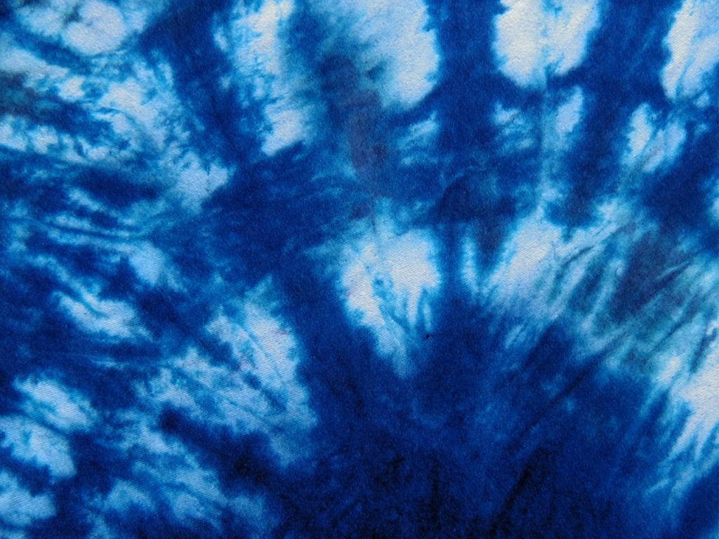 dye 桌布 壁紙 — 充滿活力的藍白紮染布料特寫，帶有漩渦狀有機圖案和紋理纖維。