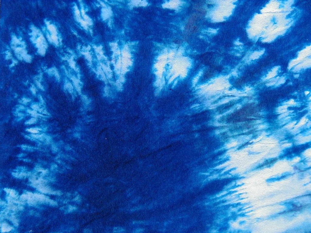dye 桌布 壁紙 — 充滿活力的藍白紮染布料特寫，帶有漩渦圖案和紋理纖維。