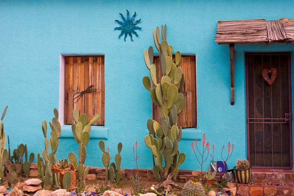Cactus 桌布 壁紙 — 充滿活力的藍綠色土坯房，配有木製百葉窗和仙人掌花園，在明亮的沙漠陽光下。