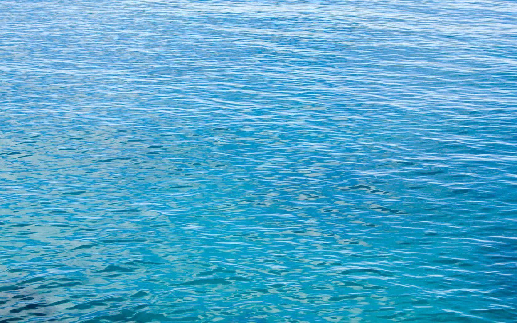 Ocean Water 桌布 壁紙 — 充滿活力的藍綠色海水在明亮的陽光下輕輕蕩漾，營造出寧靜而誘人的自然景象。