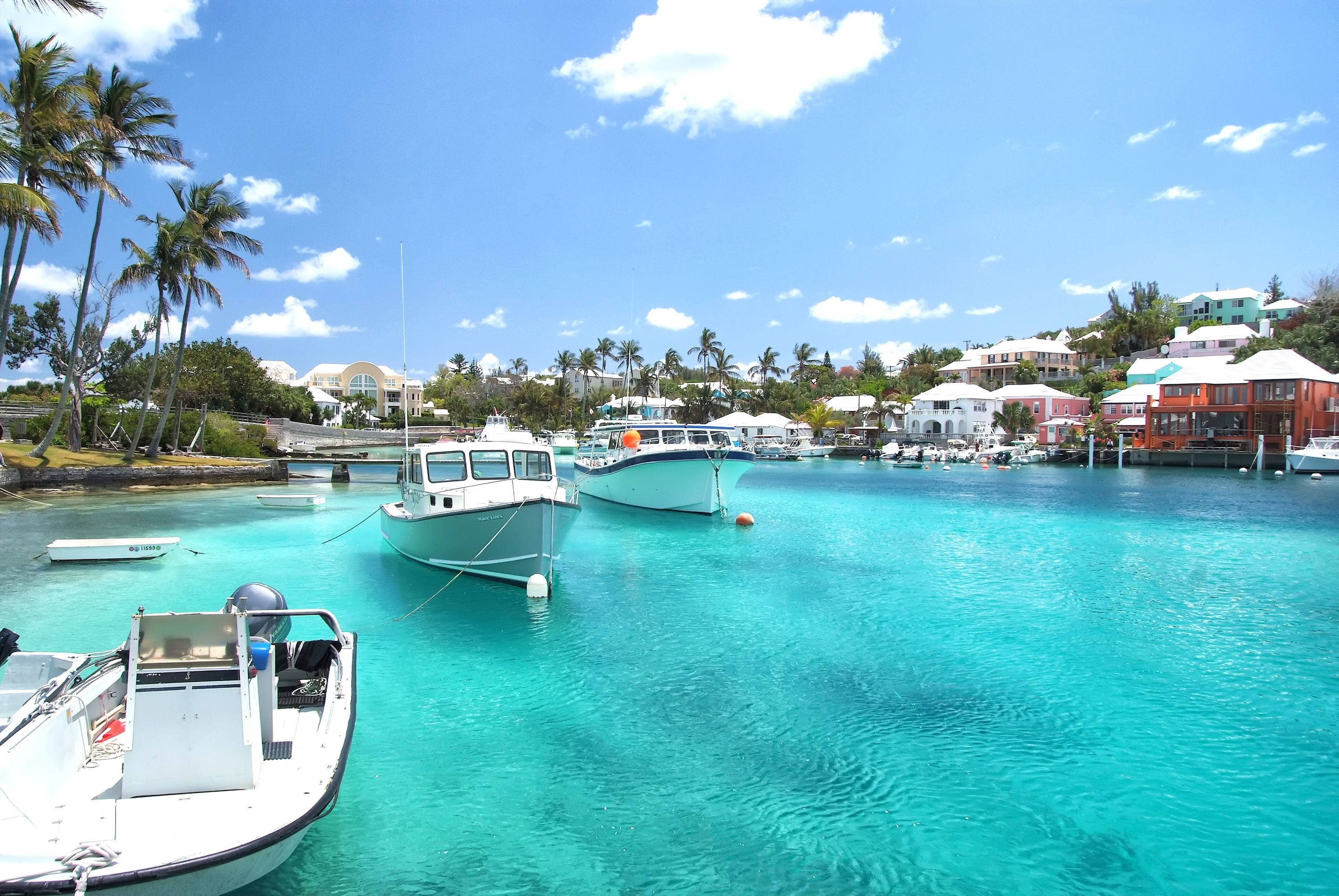 Bermuda 桌布 壁紙 — 充滿活力的藍綠色海水輕搖著錨泊的船隻，旁邊是色彩繽紛的海岸房屋，在明亮的藍天下有蓬鬆的雲朵。