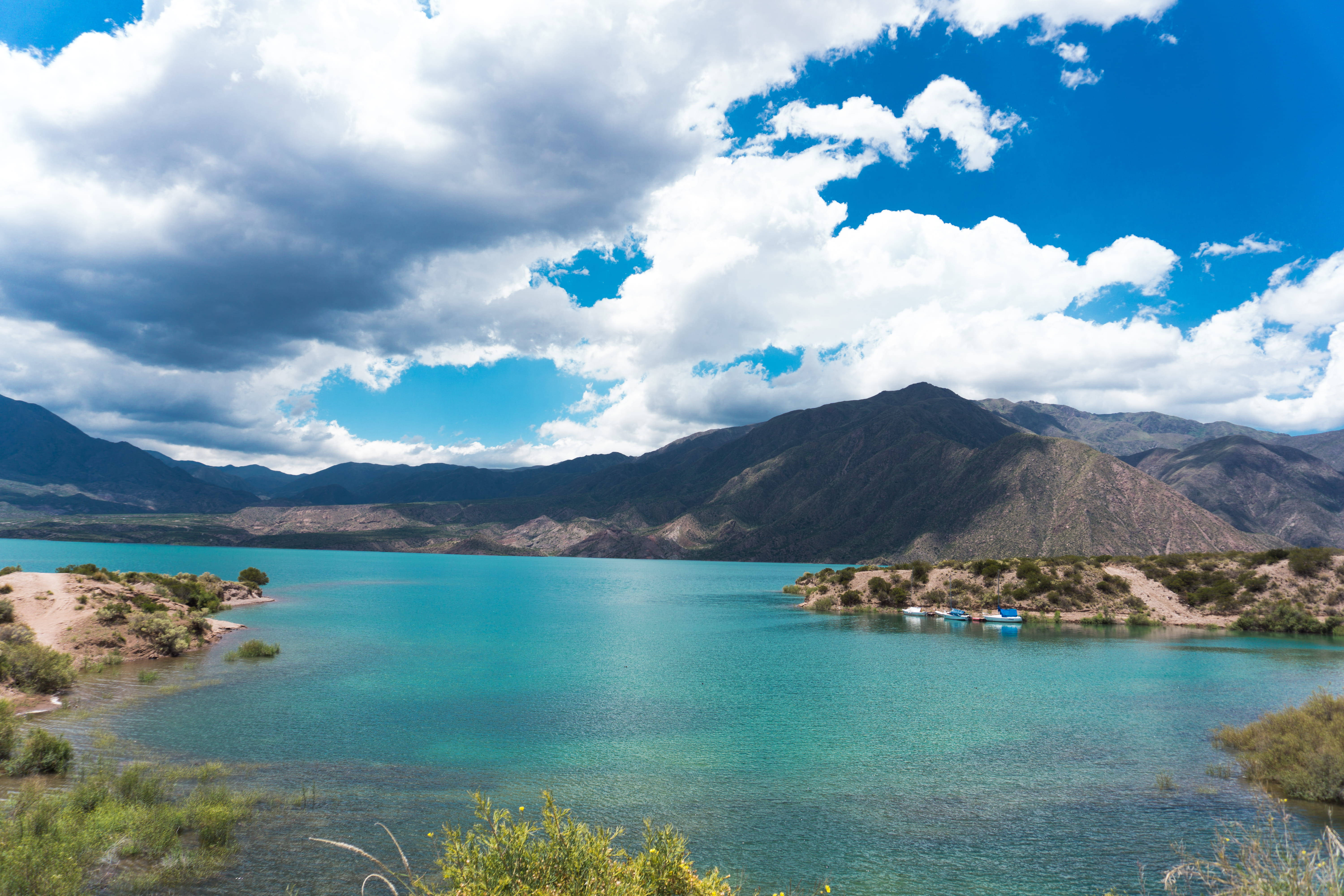 Argentina 桌布 壁紙 — 充滿活力的藍綠色湖泊坐落在崎嶇的山脈之間，上方是戲劇性的藍天和蓬鬆的白雲。