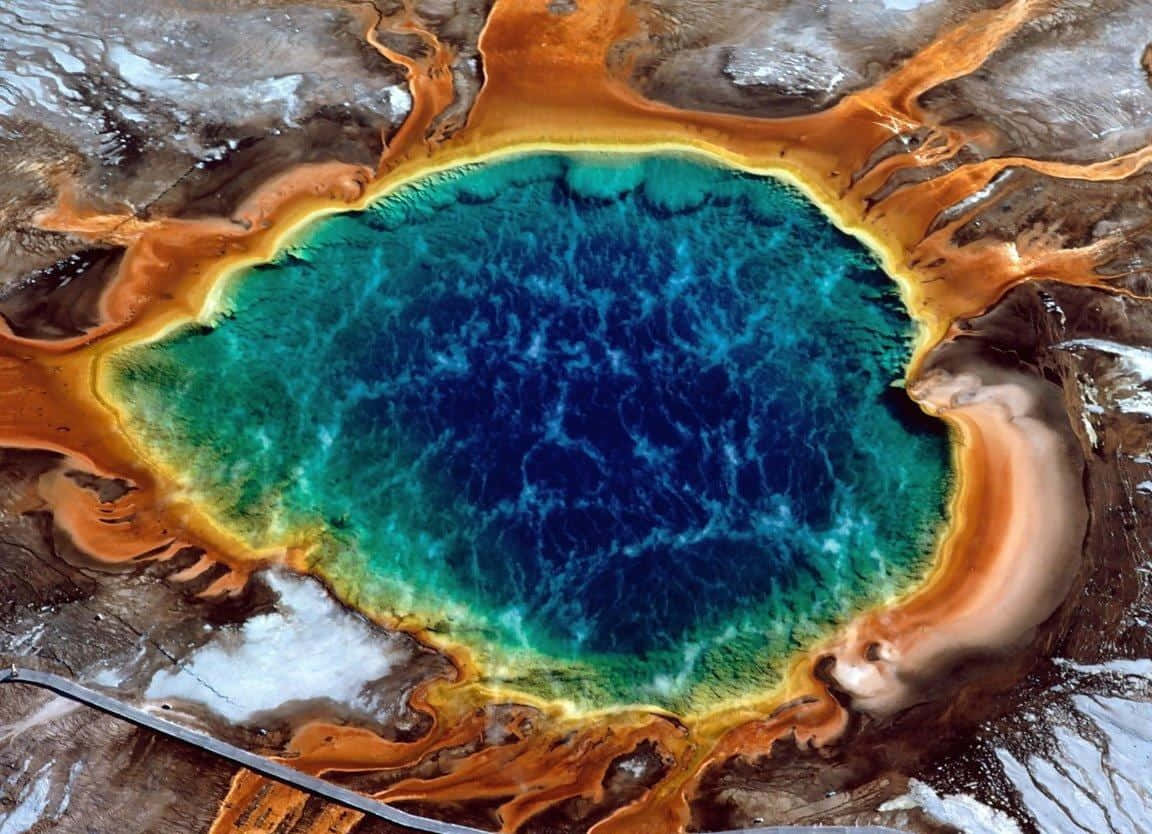 Yellowstone Geysers 桌布 壁紙 — 充滿活力的藍綠色溫泉被鐵鏽橙色礦物沉積物和雪地地形包圍的鳥瞰圖。