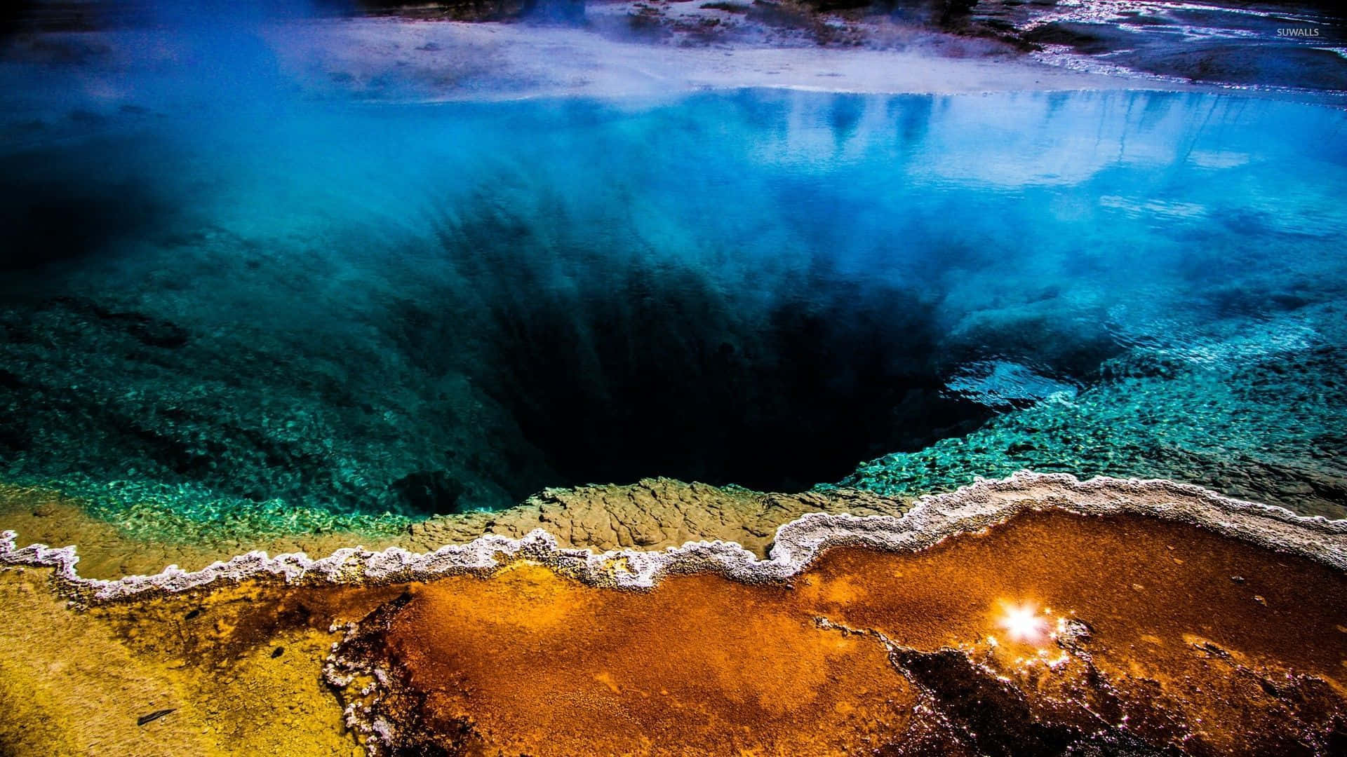 Yellowstone 桌布 壁紙 — 充滿活力的藍綠色溫泉鳥瞰圖，中心深色，礦物條紋橙色邊緣在陽光下發光。