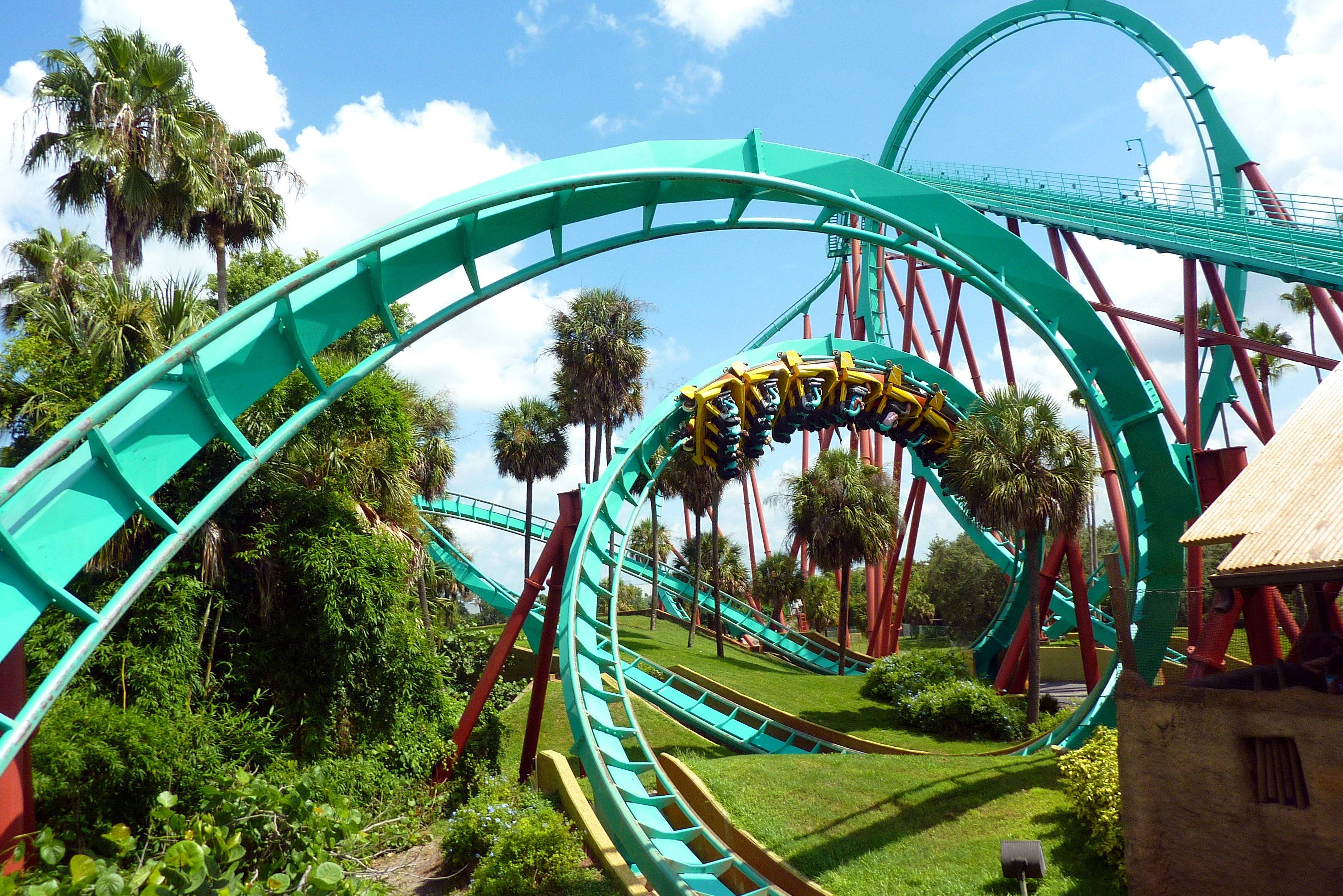 Roller Coaster 桌布 壁紙 — 充滿活力的藍綠色雲霄飛車在茂密的棕櫚樹間蜿蜒穿梭，上方是明亮的藍天和蓬鬆的白雲。