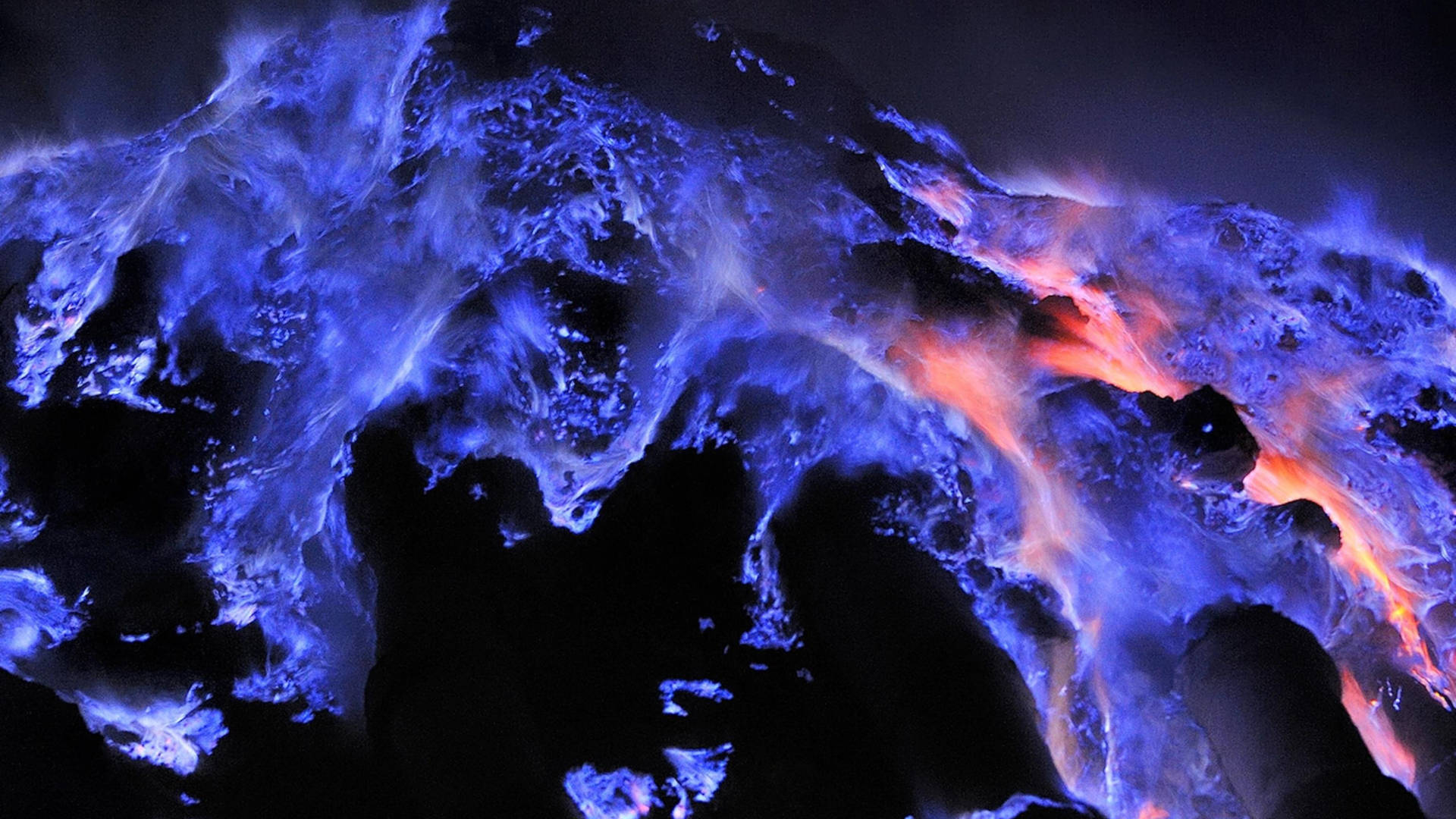 Flames 桌布 壁紙 — 充滿活力的藍色和橙色發光熔岩流在戲劇性的夜間噴發中從黑暗的火山岩上傾瀉而下。