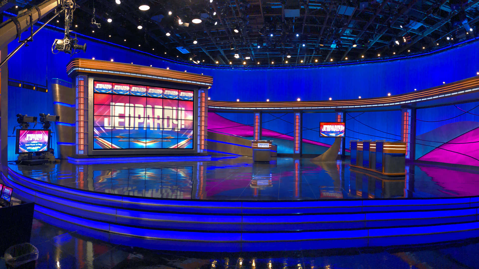 game 桌布 壁紙 — 充滿活力的藍色和粉紅色Jeopardy! 遊戲節目場景，光滑地板反射明亮的舞台燈光和大螢幕。