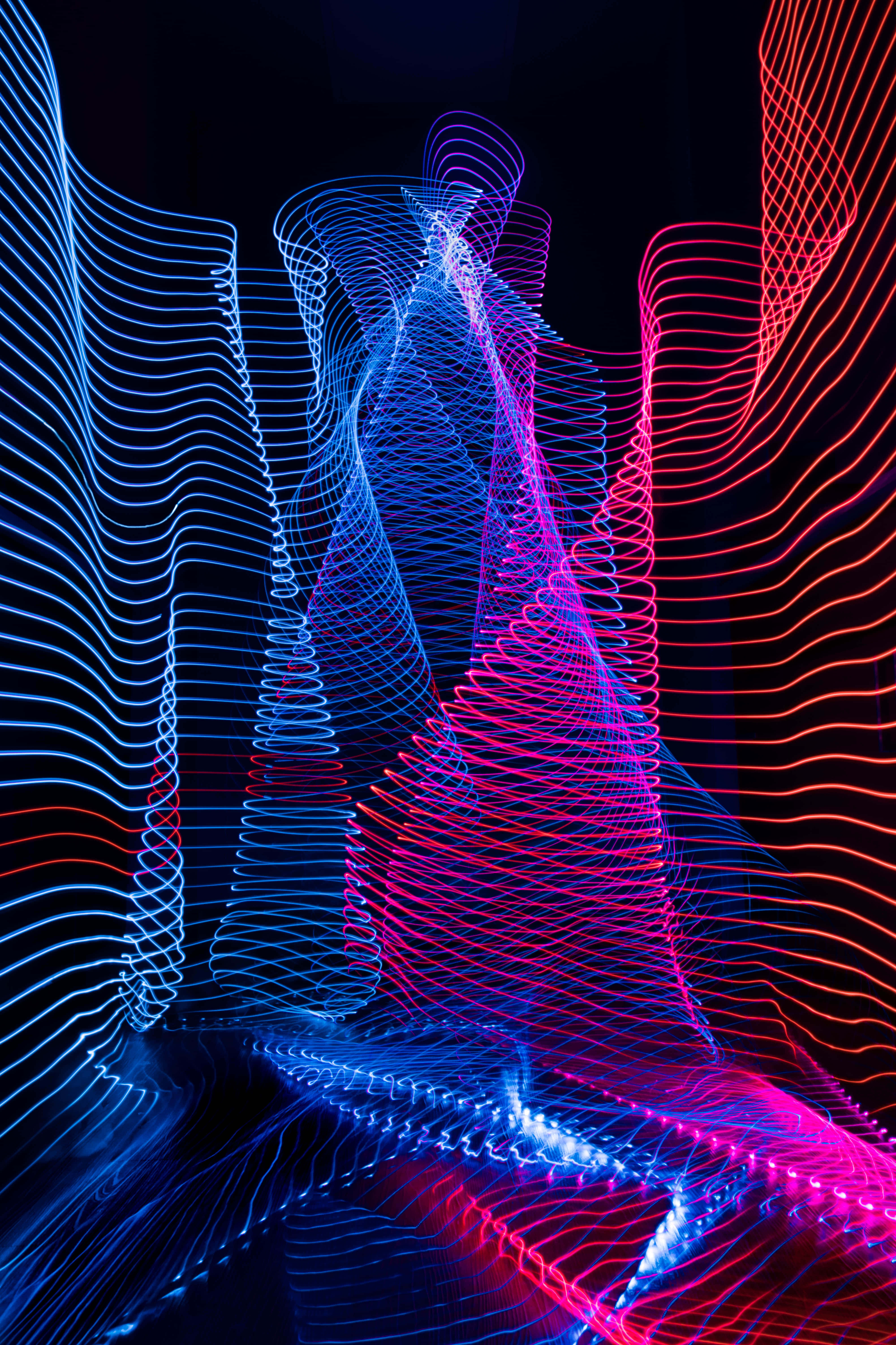 Cool Photos 桌布 壁紙 — 充滿活力的藍色和粉紅色霓虹燈軌跡在黑色背景上動態旋轉，創造出抽象的數位舞蹈。