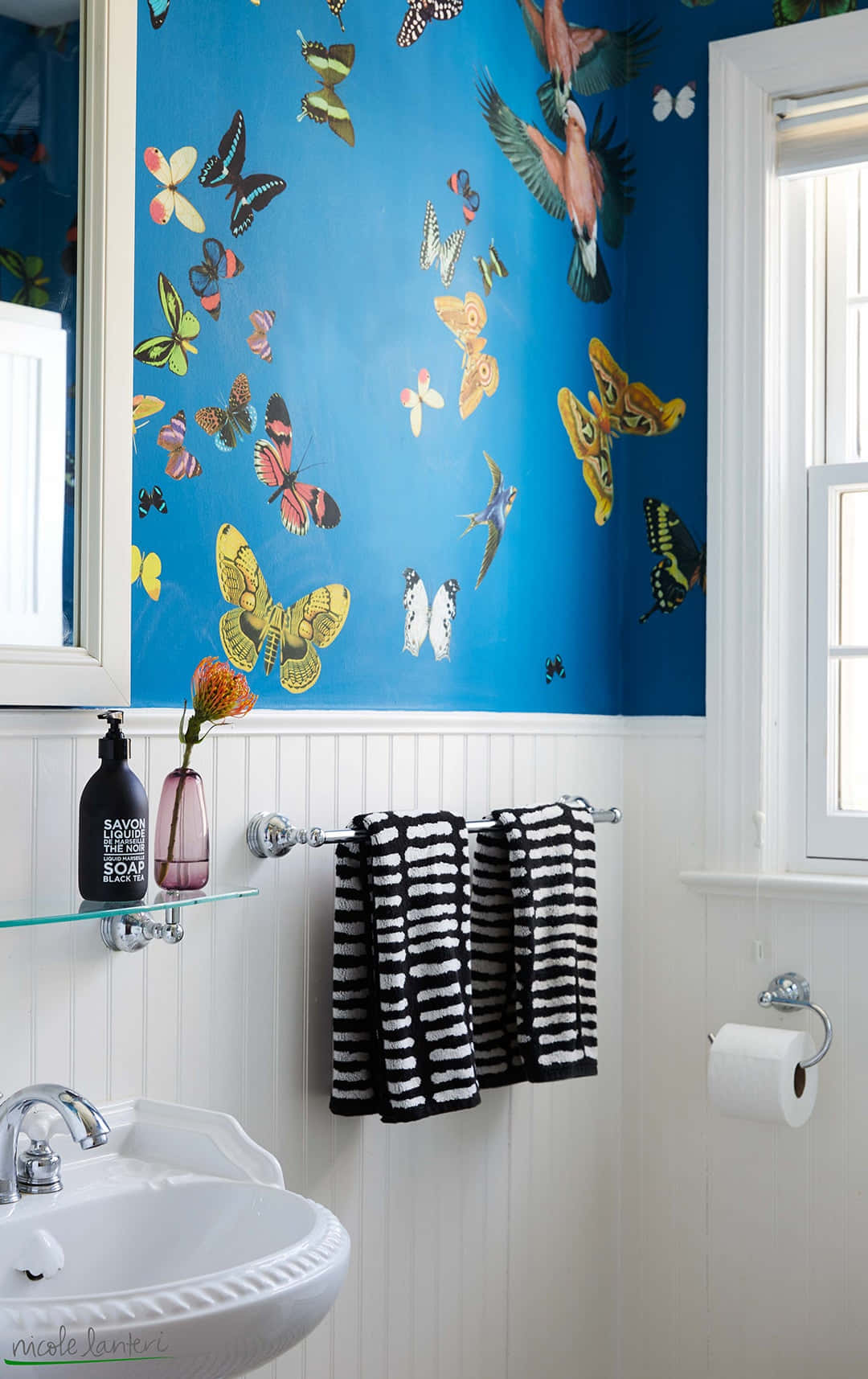 Bathroom Decor 桌布 壁紙 — 充滿活力的藍色壁紙，飾有彩色蝴蝶和鳥類，在明亮的浴室中配有白色護牆板和黑色條紋毛巾。