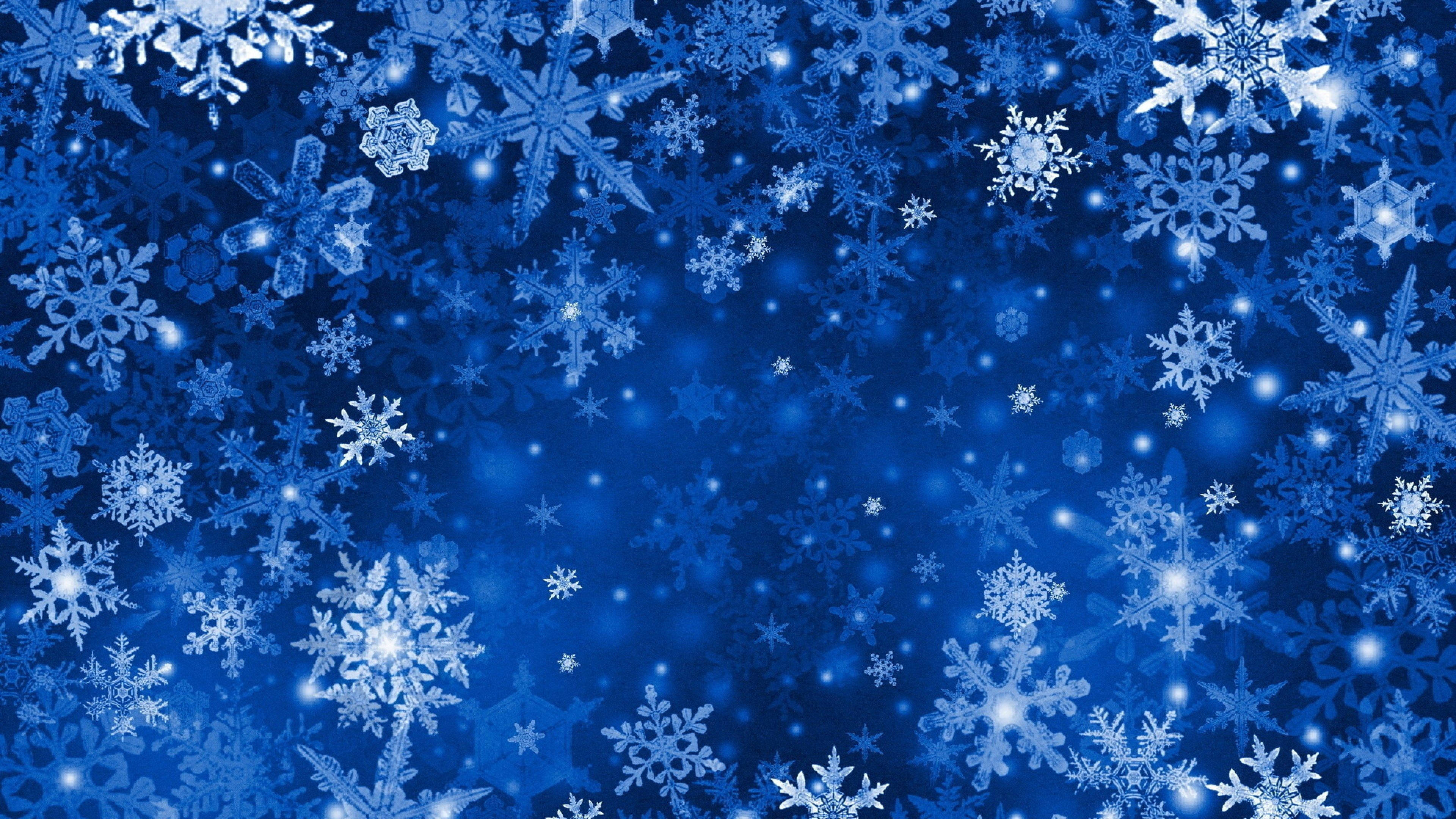雪花 桌布 壁紙 — 充滿活力的藍色背景上，各種精緻設計的發光白色雪花輕輕飄浮。