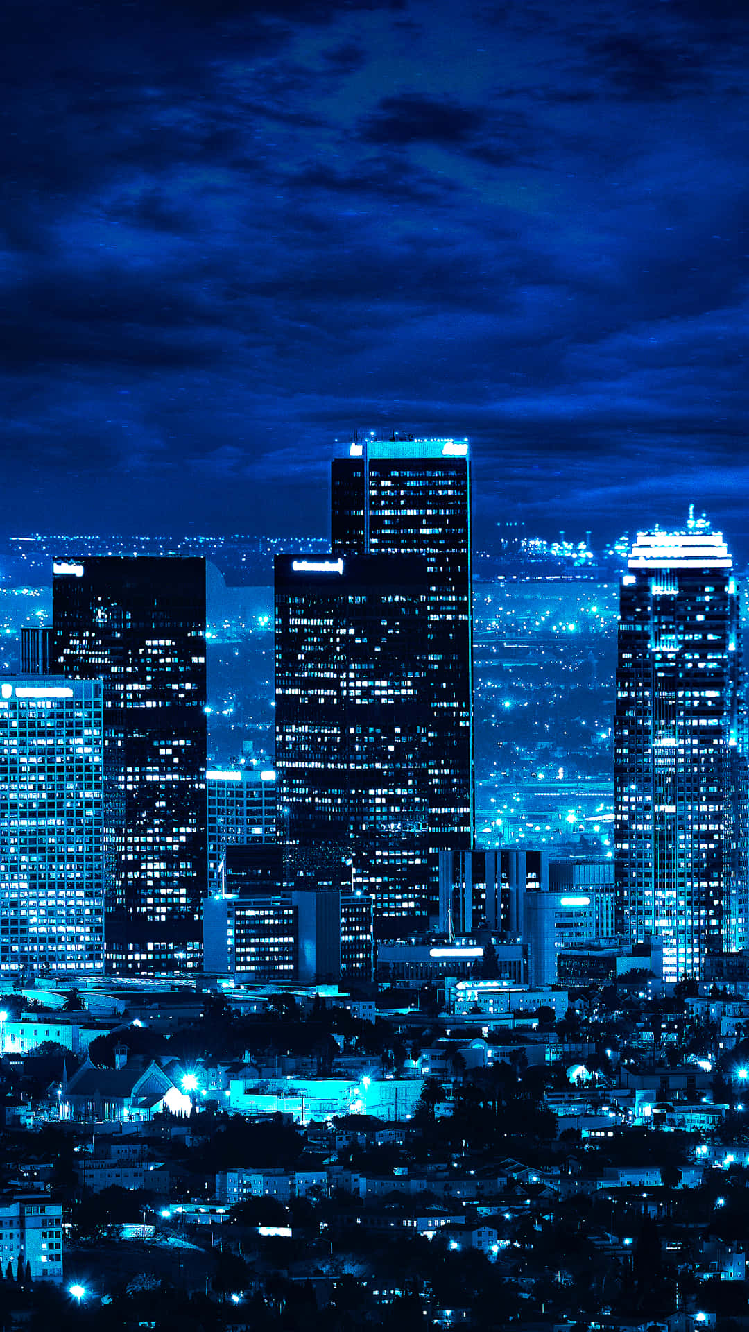 城市 桌布 壁紙 — 充滿活力的藍色調夜景，高聳的摩天大樓在多雲的天空下閃耀。