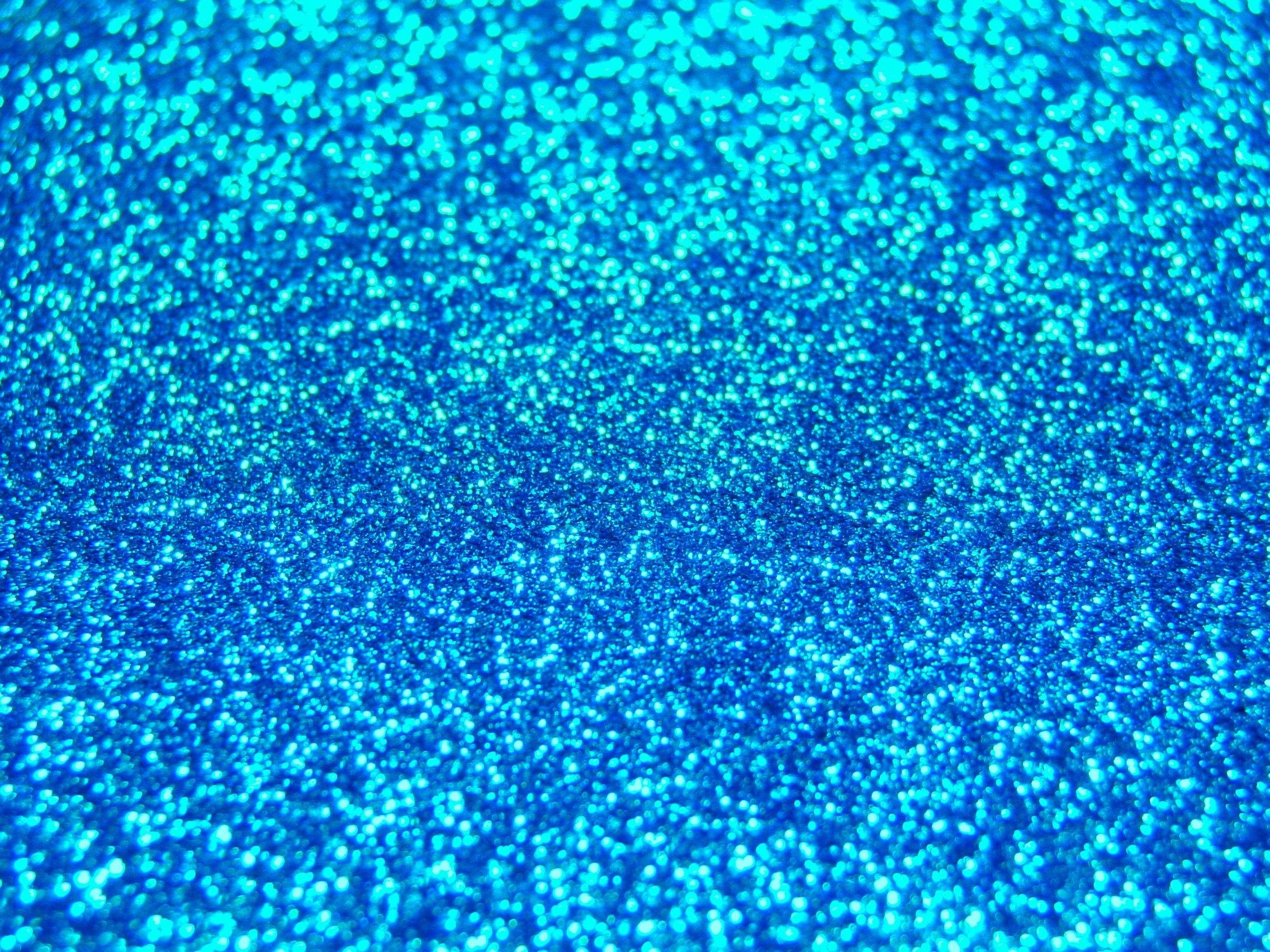 Holographic 桌布 壁紙 — 充滿活力的藍色閃粉特寫，閃爍的顆粒在光線下形成紋理閃爍的圖案。