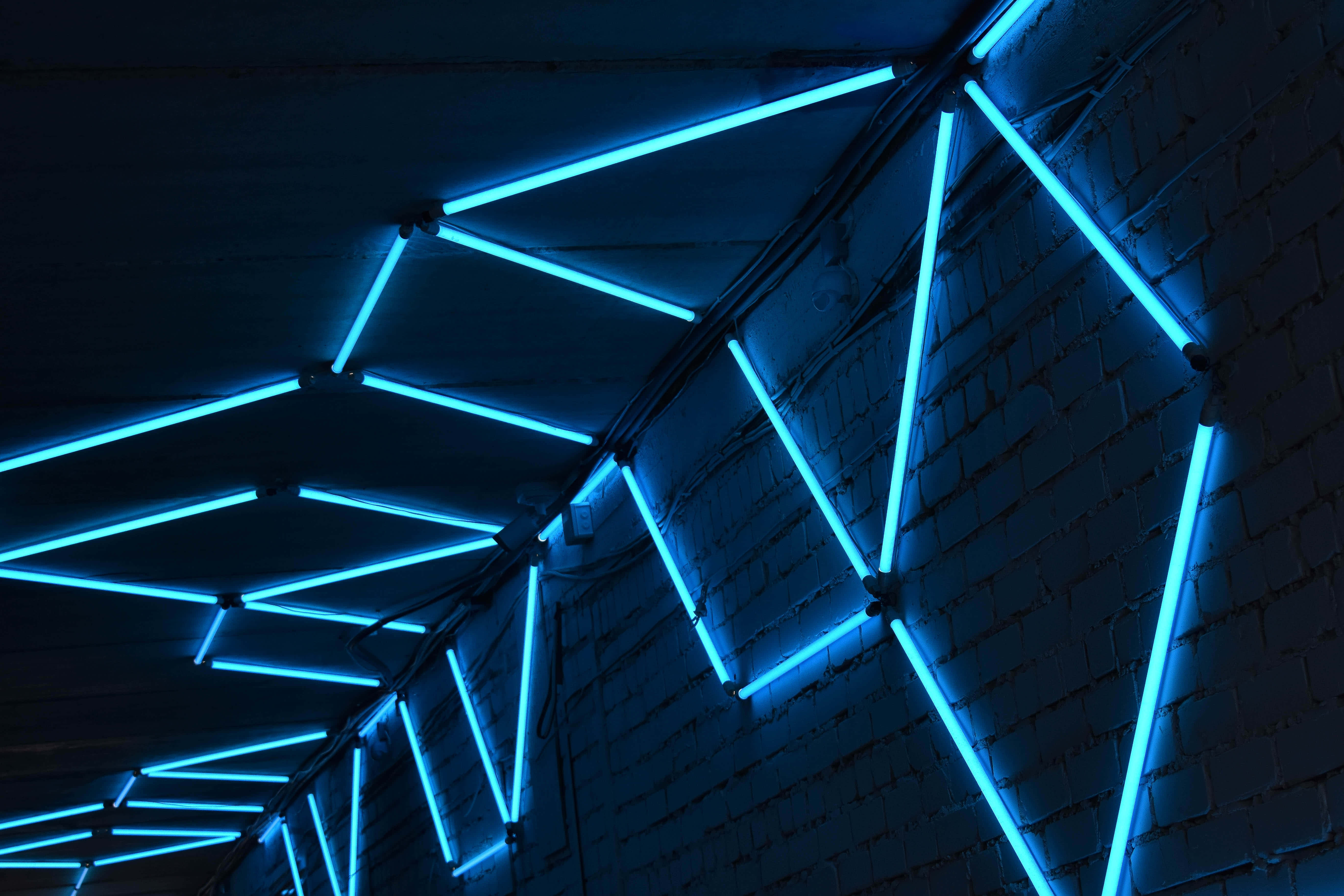 Blue Neon Lights 桌布 壁紙 — 充滿活力的藍色霓虹燈管在現代工業環境中，於深色磚牆和天花板上形成幾何圖案。