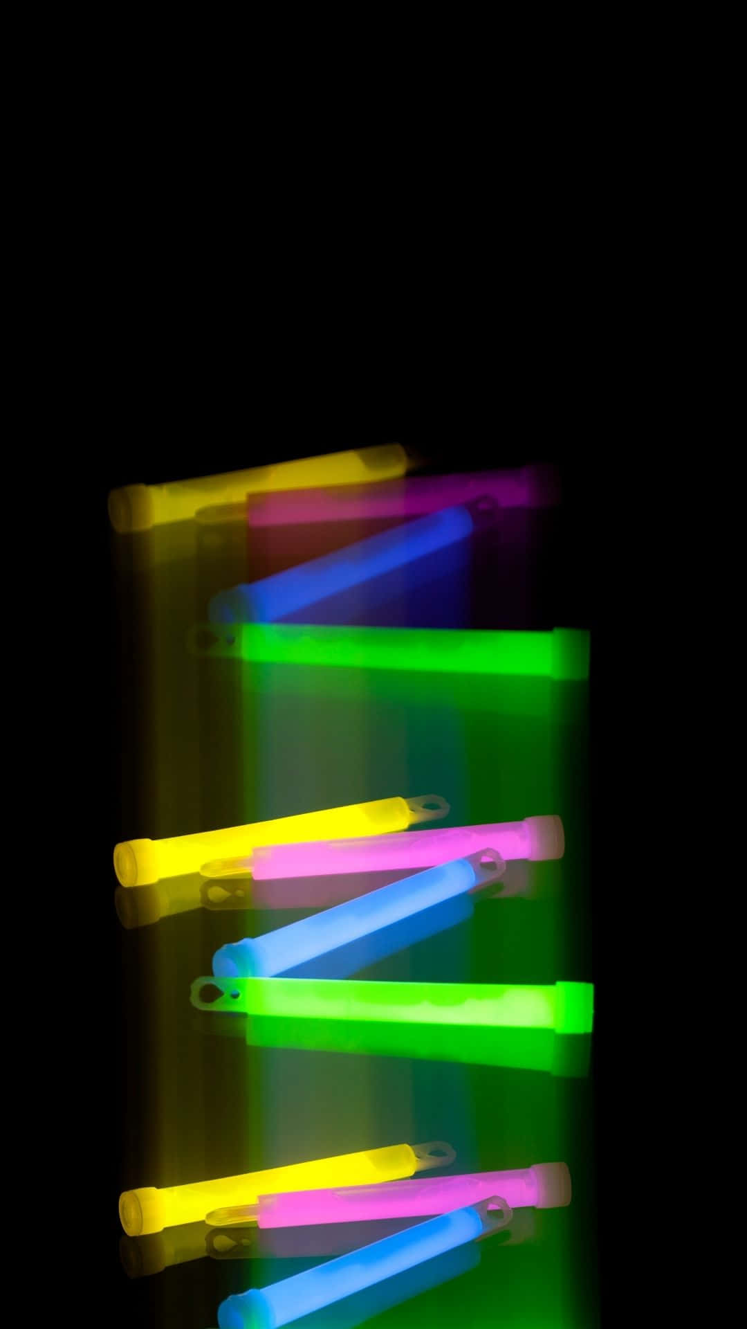 Glow In The Dark 桌布 壁紙 — 充滿活力的螢光棒，顏色有黃色、粉紅色、藍色和綠色，以對角線排列在黑色背景上，帶有柔和反射。