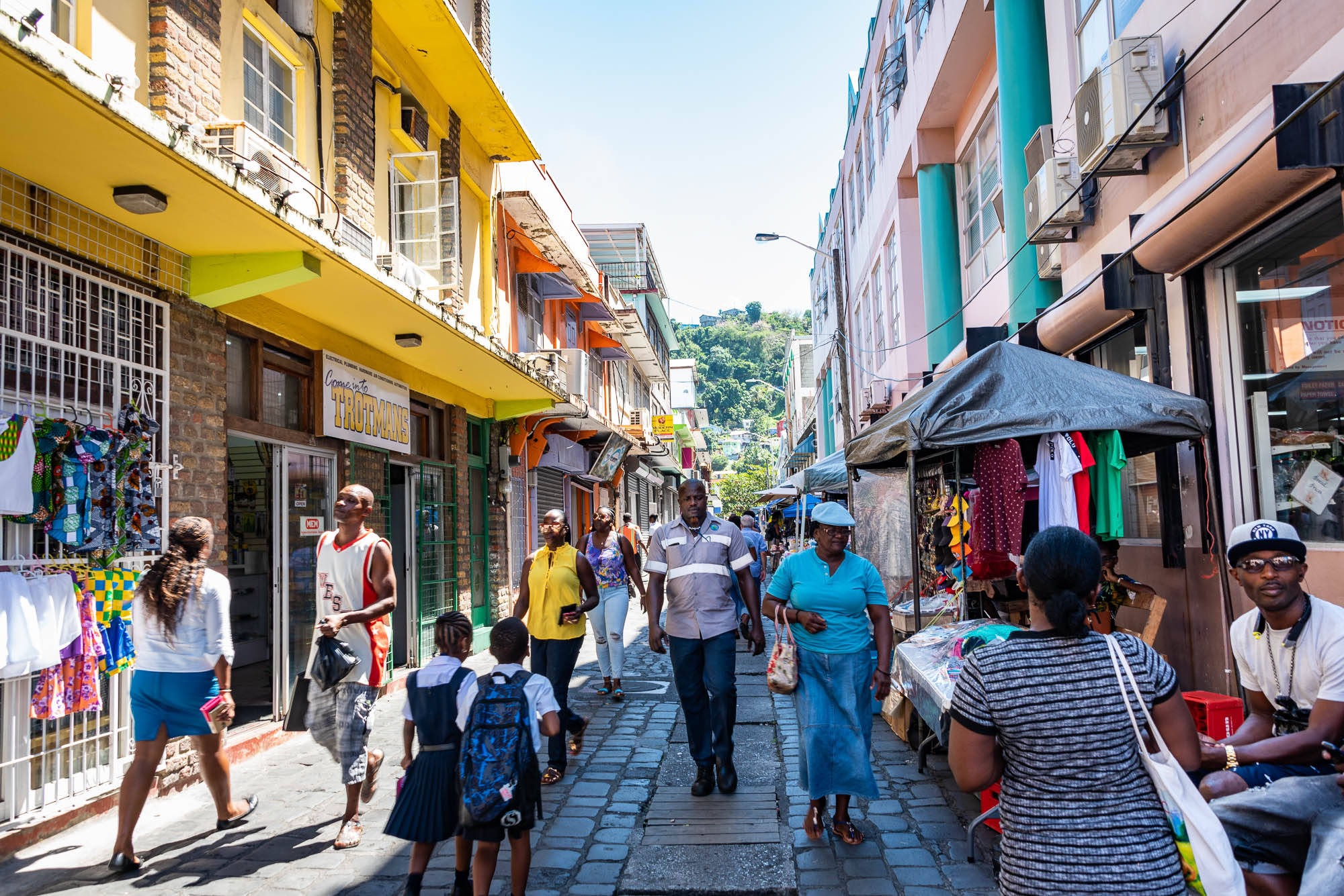 St Vincent And The Grenadines 桌布 壁紙 — 充滿活力的街景，行人走過色彩繽紛的商店門面和市場攤位，在明亮的日光下。