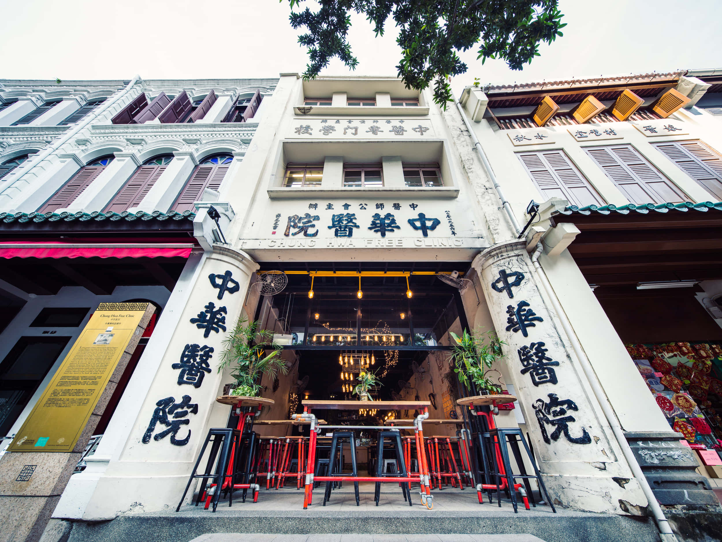 awesome cool 桌布 壁紙 — 充滿活力的街頭景觀，歷史悠久的店屋柱子上有中文字，現代酒吧外有紅色凳子。