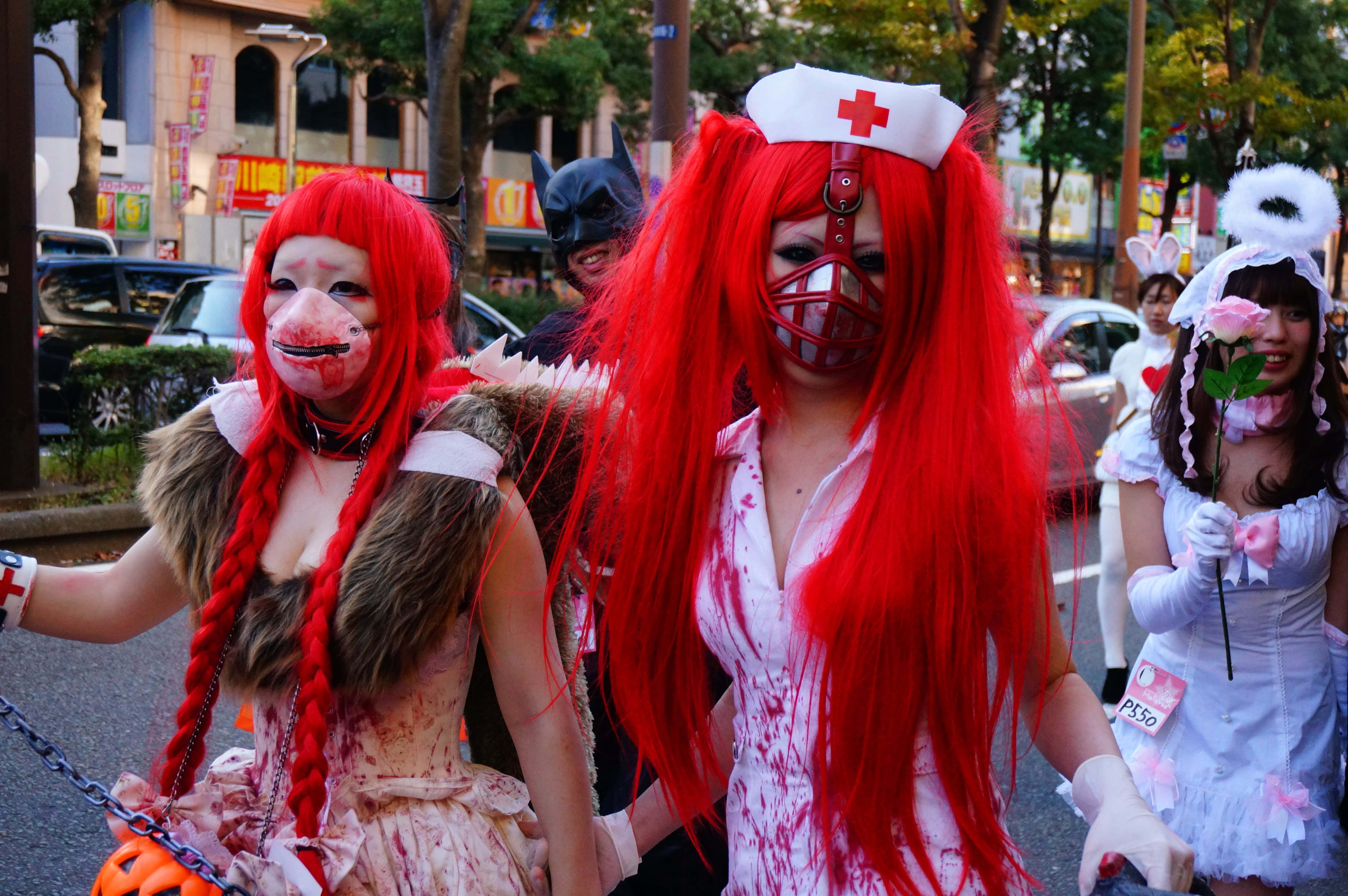Halloween Parades 桌布 壁紙 — 充滿活力的街頭遊行，扮演者穿著血淋淋的護士和豬面具服裝，搭配紅色假髮和血濺效果。