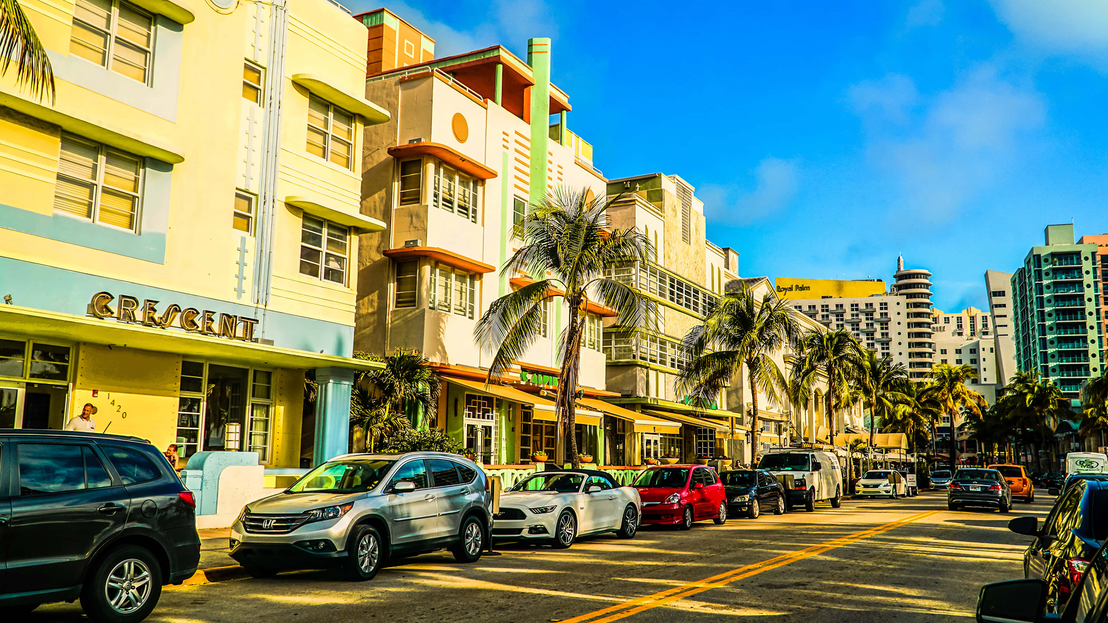 Miami 桌布 壁紙 — 充滿活力的裝飾藝術建築排列在陽光明媚的邁阿密街道上，棕櫚樹和停放的汽車在清澈的藍天下。