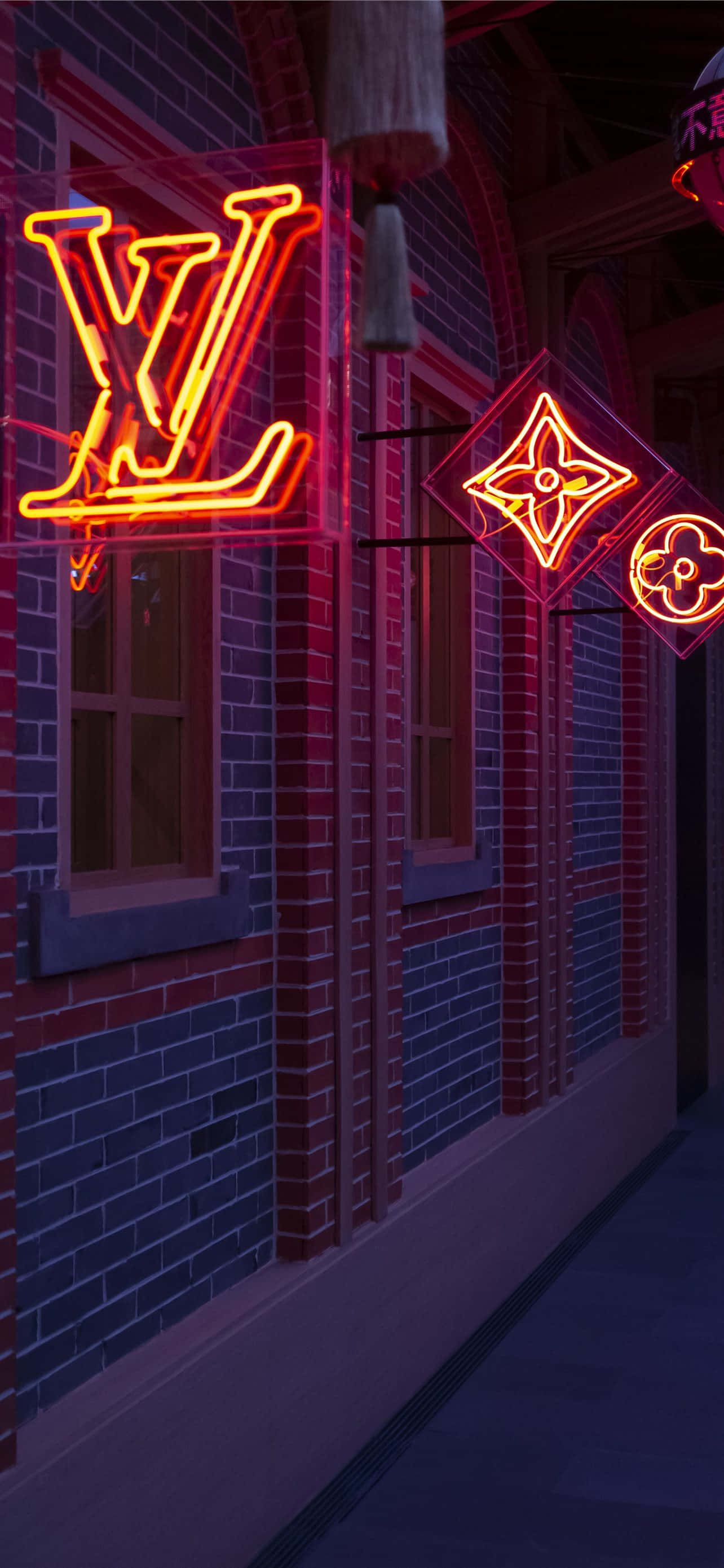 Louis Vuitton Logo 桌布 壁紙 — 充滿活力的路易威登霓虹招牌在夜間映照著磚牆建築外牆，在潮濕的路面上投射出色彩繽紛的倒影。