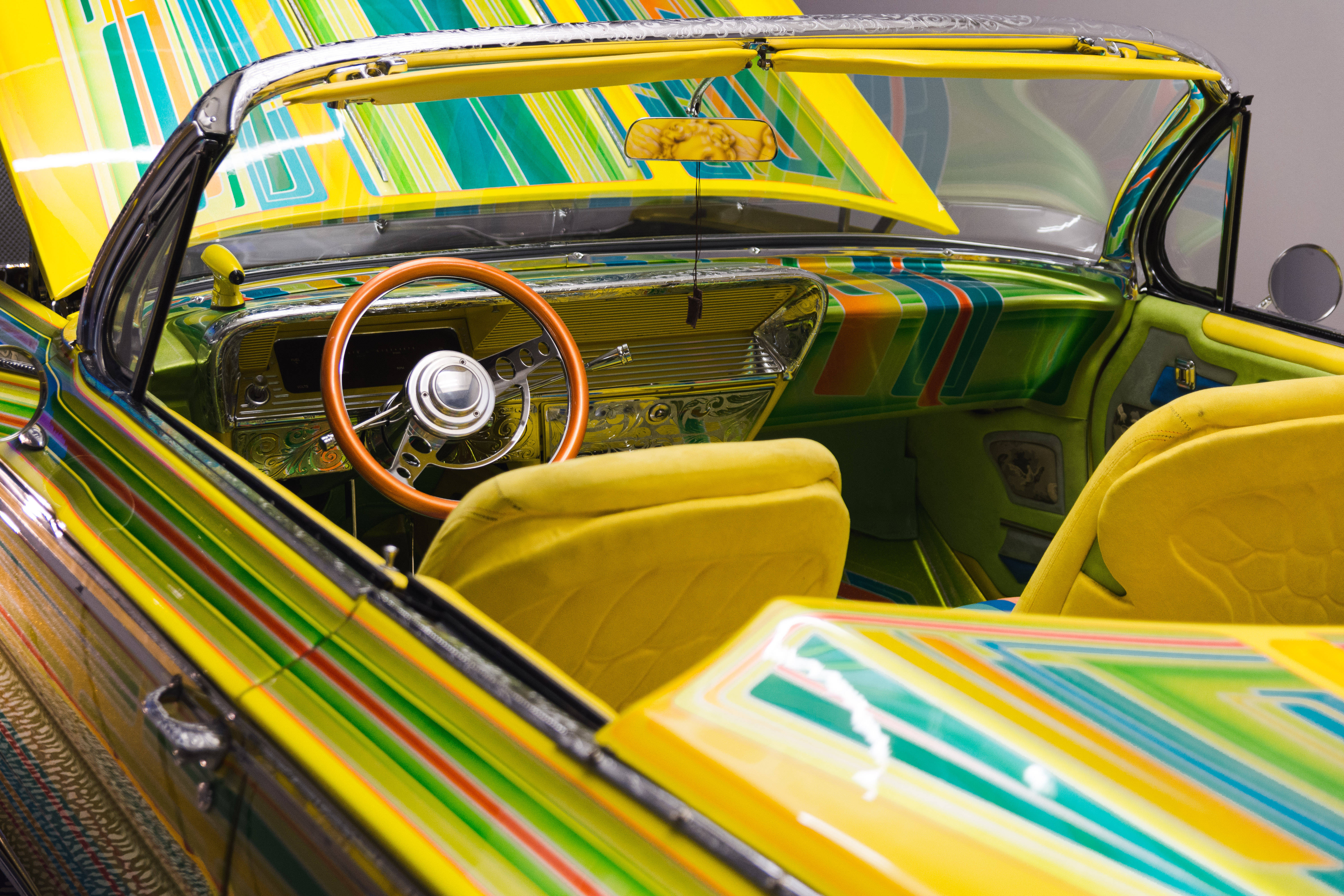 Lowrider 桌布 壁紙 — 充滿活力的迷幻條紋覆蓋經典敞篷車的內外，配備黃色座椅和木質方向盤。
