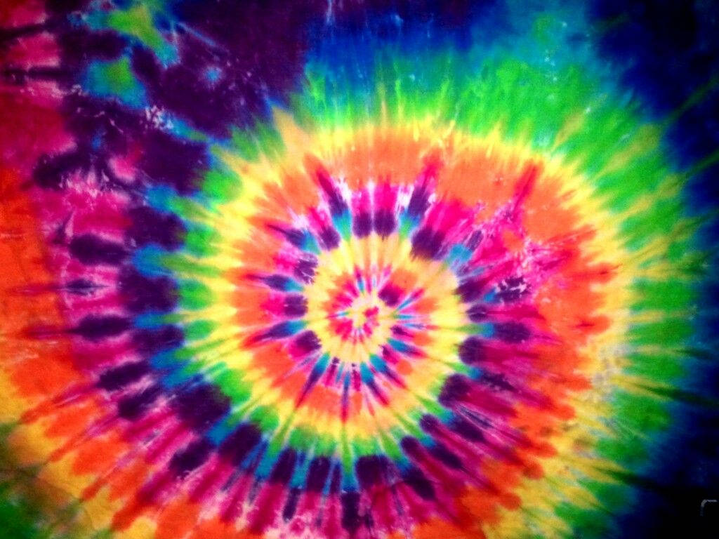 dye 桌布 壁紙 — 充滿活力的迷幻紮染螺旋從色彩繽紛的中心散發出來，彩虹色調融入深紫色邊緣。