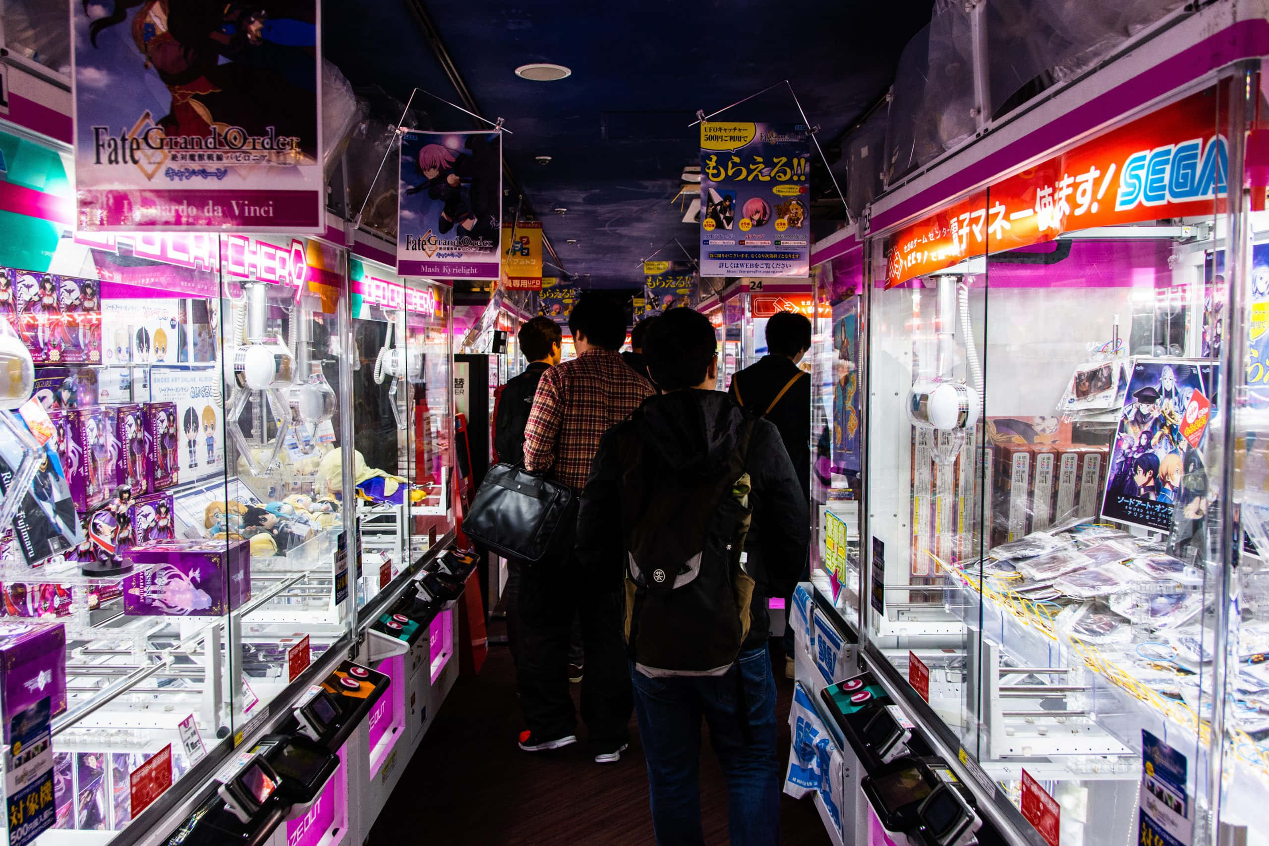 Otaku Culture 桌布 壁紙 — 充滿活力的遊戲機走廊，兩旁擺滿發光的夾娃娃機，裡面裝滿動漫人偶和商品，上方是色彩繽紛的霓虹招牌。