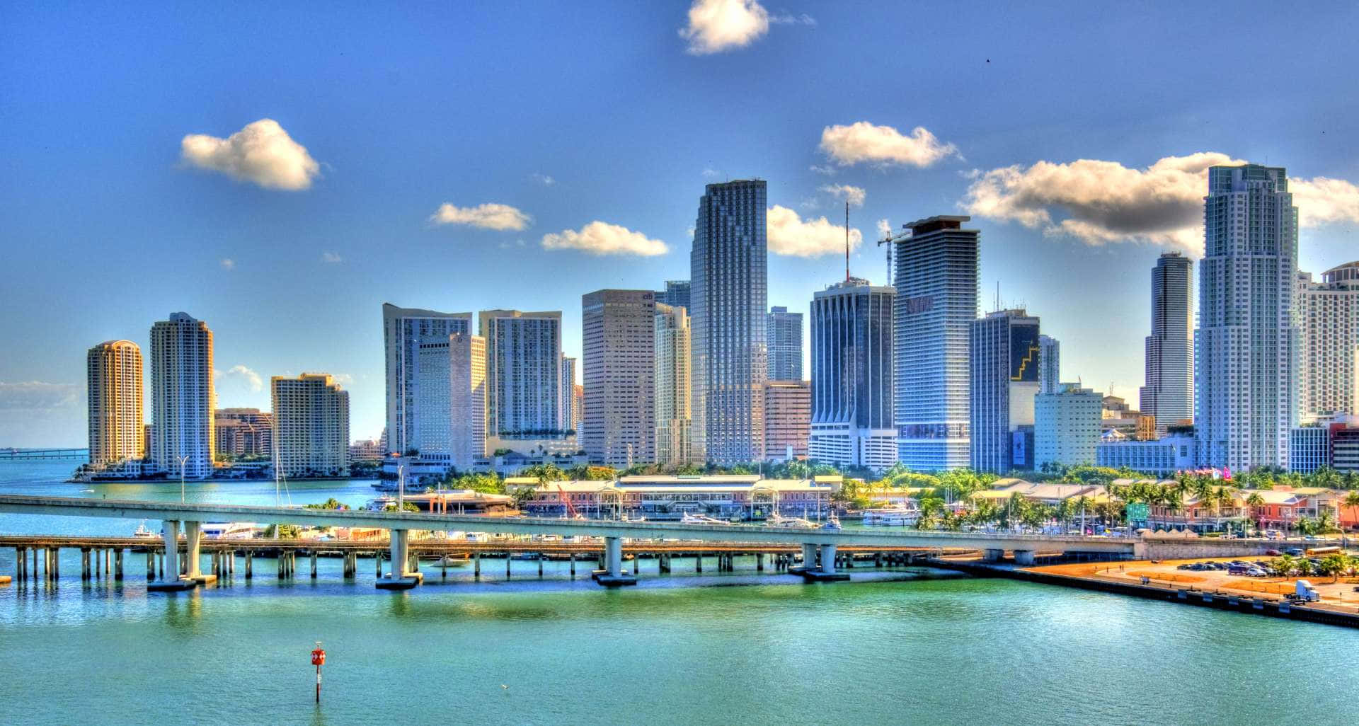 Miami 桌布 壁紙 — 充滿活力的邁阿密天際線，玻璃摩天大樓在碧綠的水面和橋樑上反射陽光。