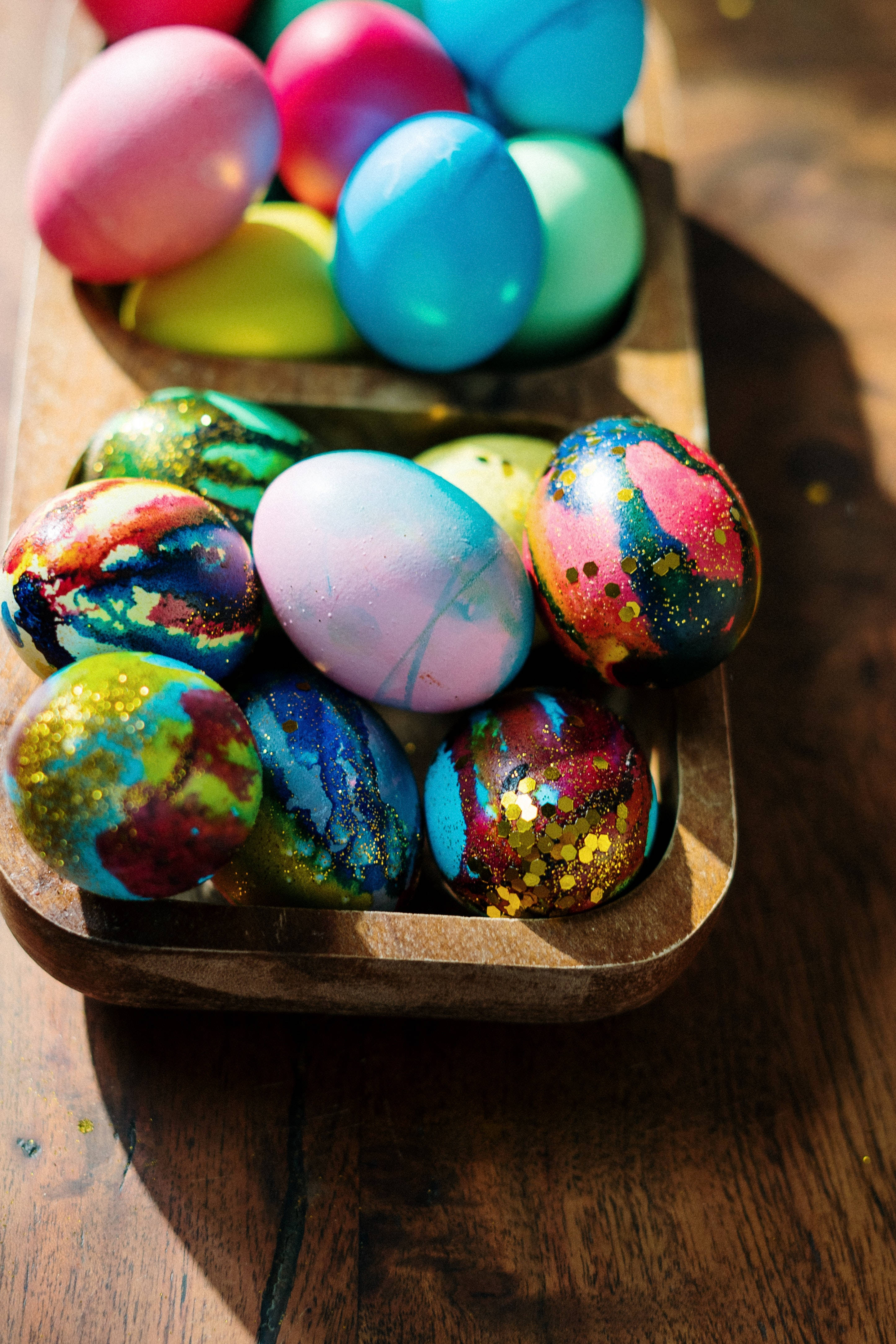 Happy Easter 桌布 壁紙 — 充滿活力的雲石紋和閃粉復活節蛋放在木托盤上，沐浴在溫暖的陽光中，置於質樸的木桌上。