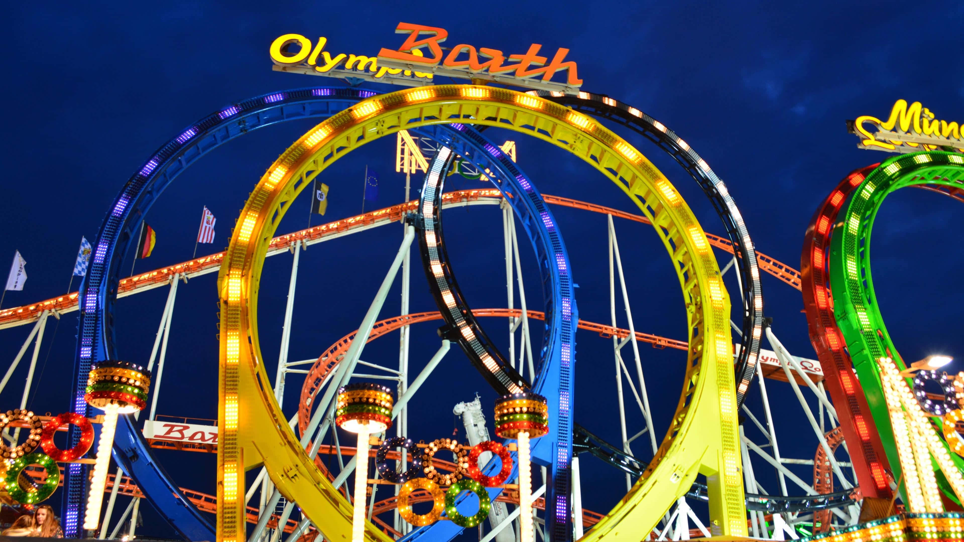 Roller Coaster 桌布 壁紙 — 充滿活力的雲霄飛車，帶有發光的環圈和霓虹燈，照亮了夜間驚險刺激的遊樂園。