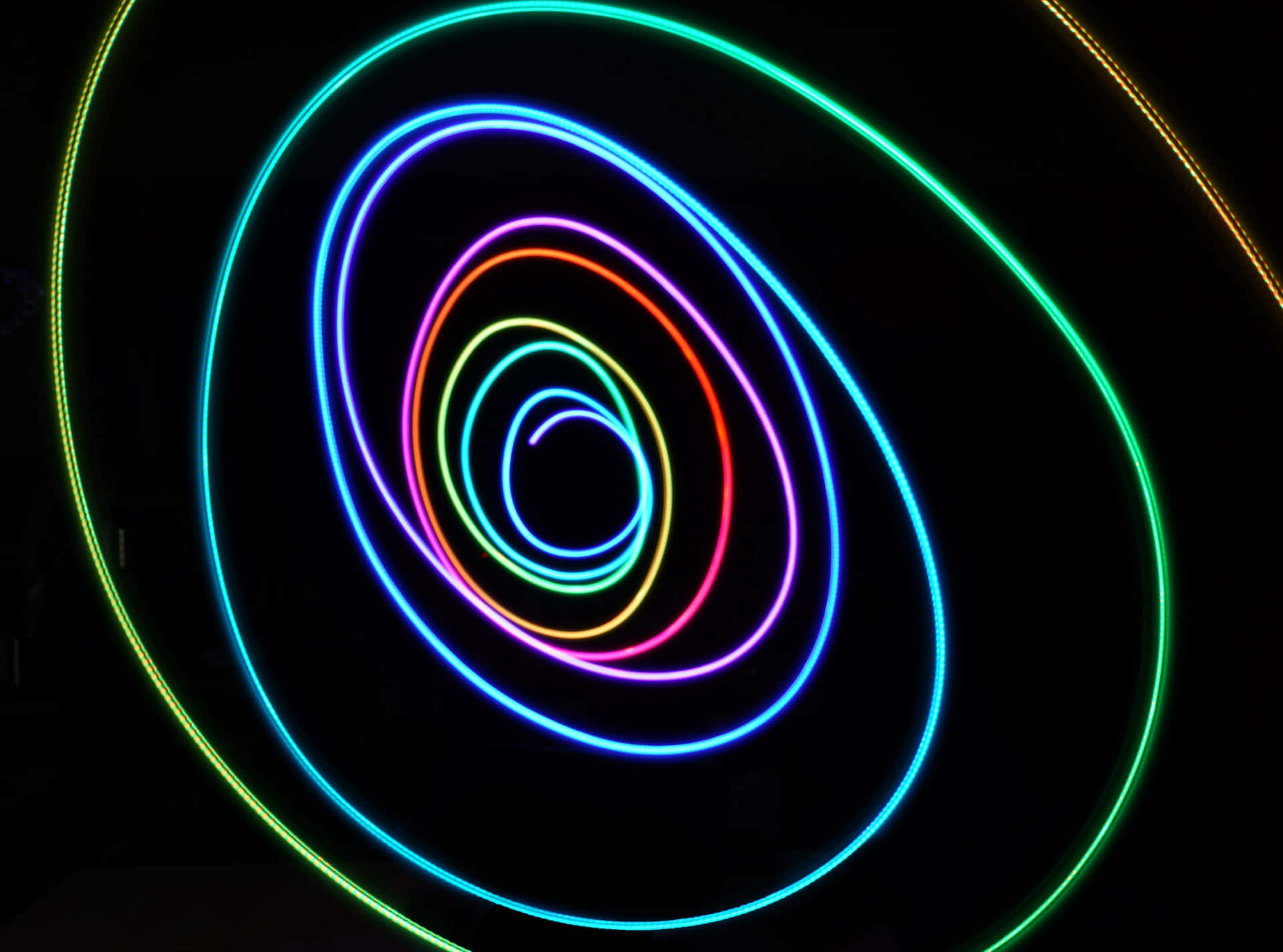 Psychedelic Neon Lights 桌布 壁紙 — 充滿活力的霓虹圈在漆黑背景下向內螺旋，營造出催眠般的發光漩渦效果。