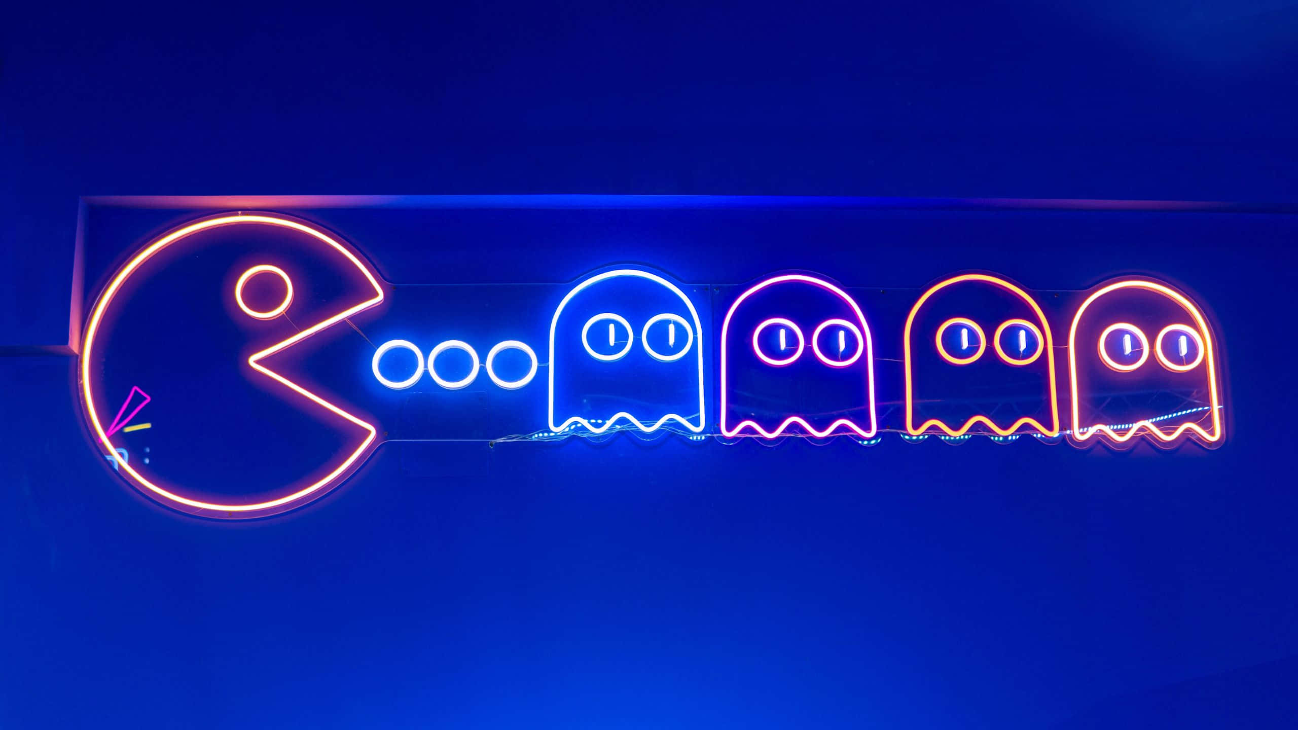 Gaming Banner 桌布 壁紙 — 充滿活力的霓虹燈 Pac-Man 和鬼魂在深藍色牆壁上以復古街機風格發光。