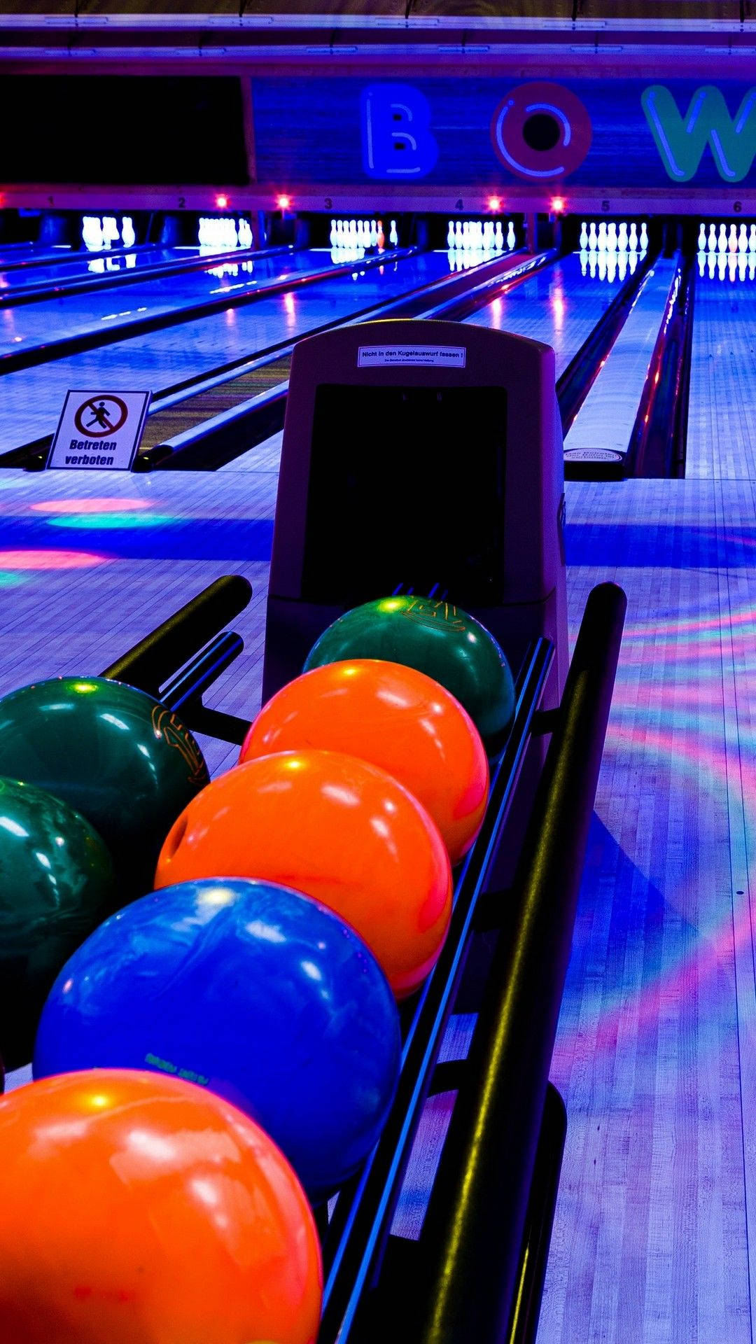 Bowling 桌布 壁紙 — 充滿活力的霓虹燈保齡球館，前景有色彩繽紛的保齡球，球道延伸至發光的遠方。