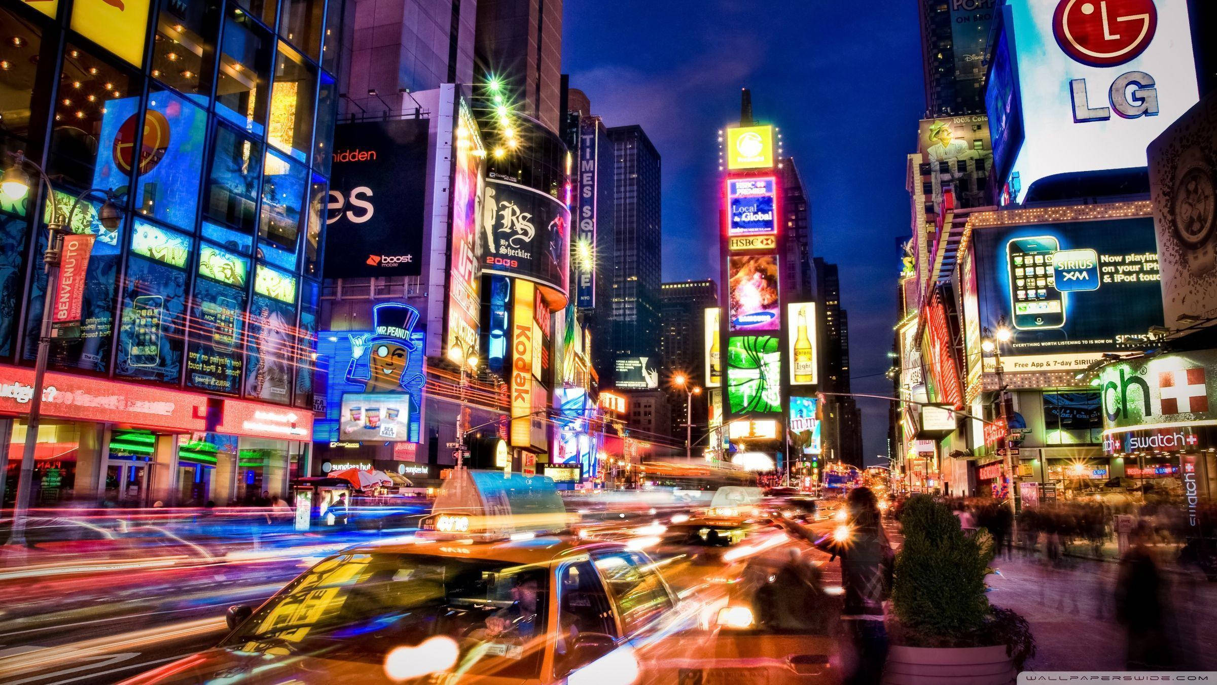Broadway 桌布 壁紙 — 充滿活力的霓虹燈光劃過夜晚繁忙的城市街道，伴隨著模糊的車流和高聳的廣告牌。