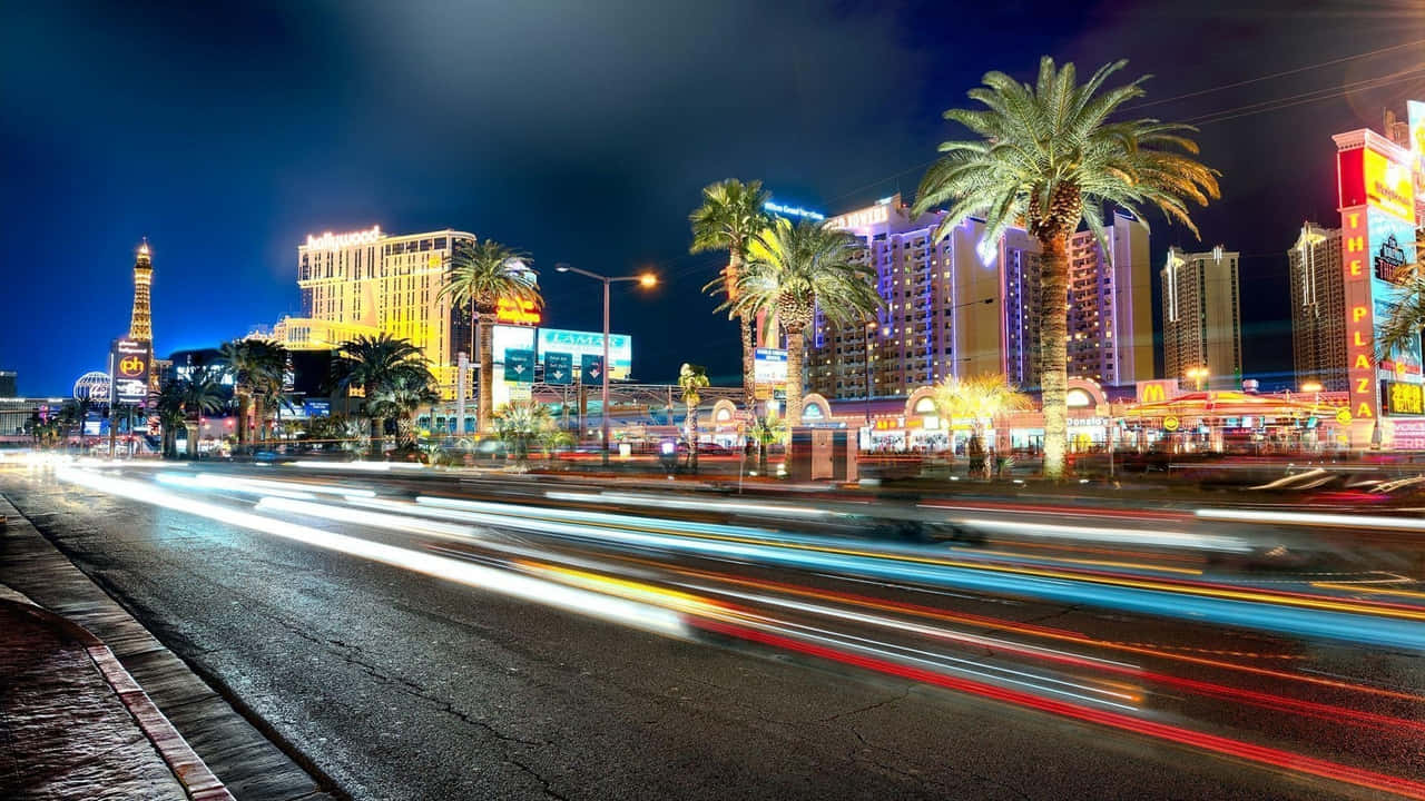 720p Las Vegas 桌布 壁紙 — 充滿活力的霓虹燈光在夜間劃過繁華的拉斯維加斯大道，棕櫚樹和高聳的酒店在黑暗的天空下閃耀。