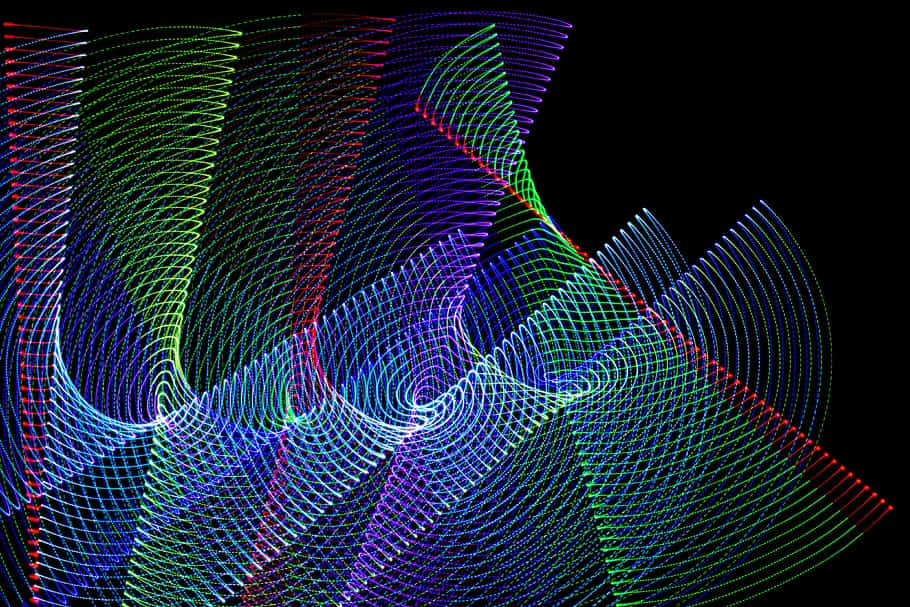 RGB 桌布 壁紙 — 充滿活力的霓虹燈光軌跡在漆黑的背景上以催眠般的圖案旋轉，創造出動態的數位抽象。
