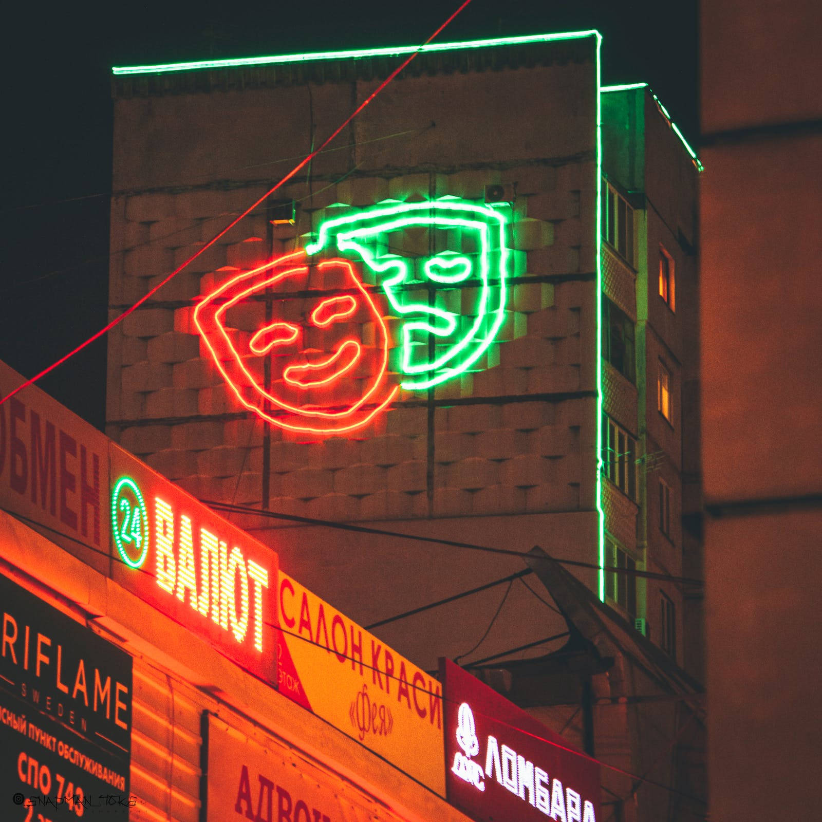 Neon Phone 桌布 壁紙 — 充滿活力的霓虹燈劇院面具在夜晚的黑暗城市建築外牆上發出紅色和綠色的光芒。