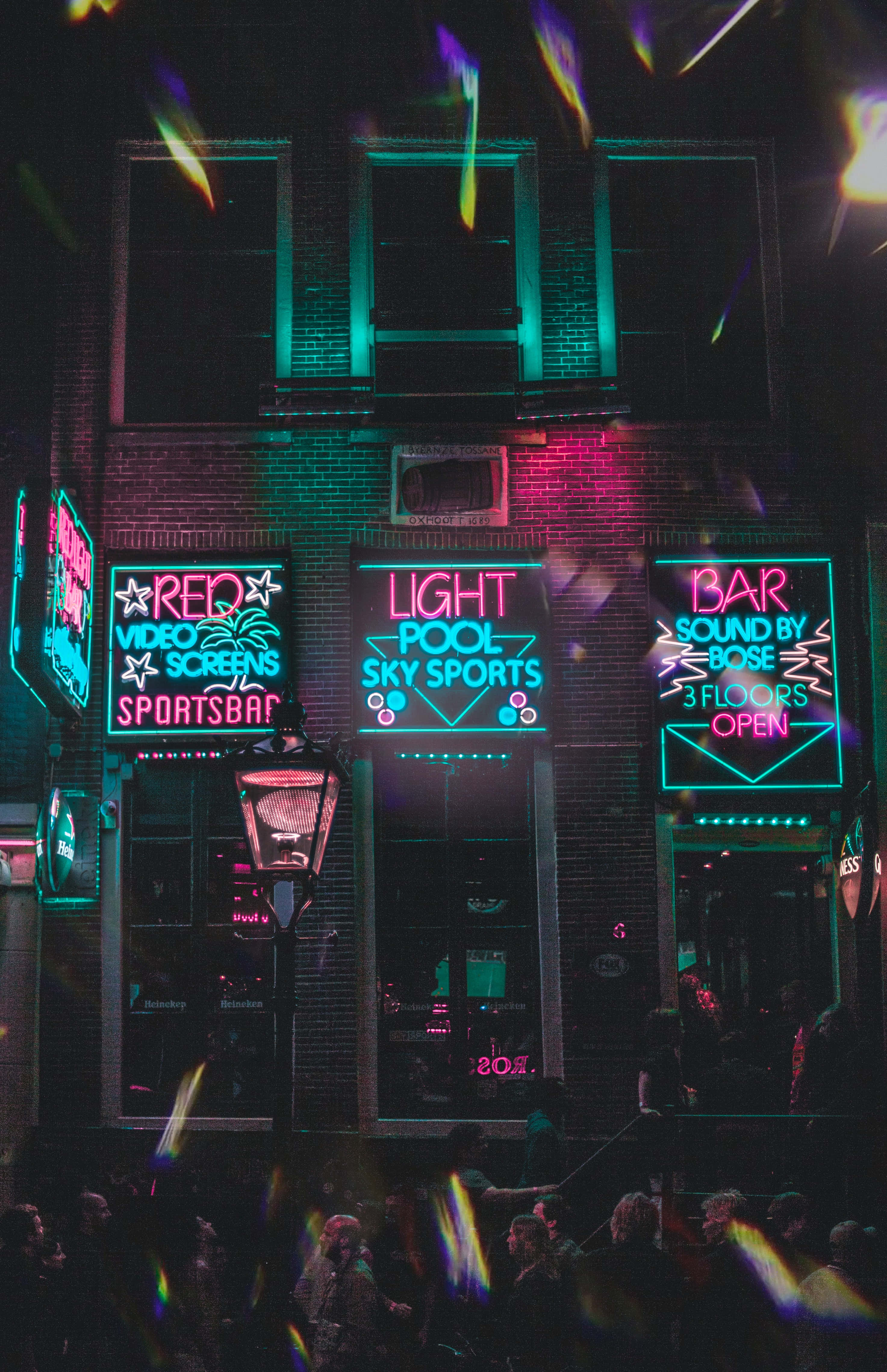 Nightclub 桌布 壁紙 — 充滿活力的霓虹燈在夜晚的磚砌建築上閃耀，人群在色彩繽紛的光線下聚集。