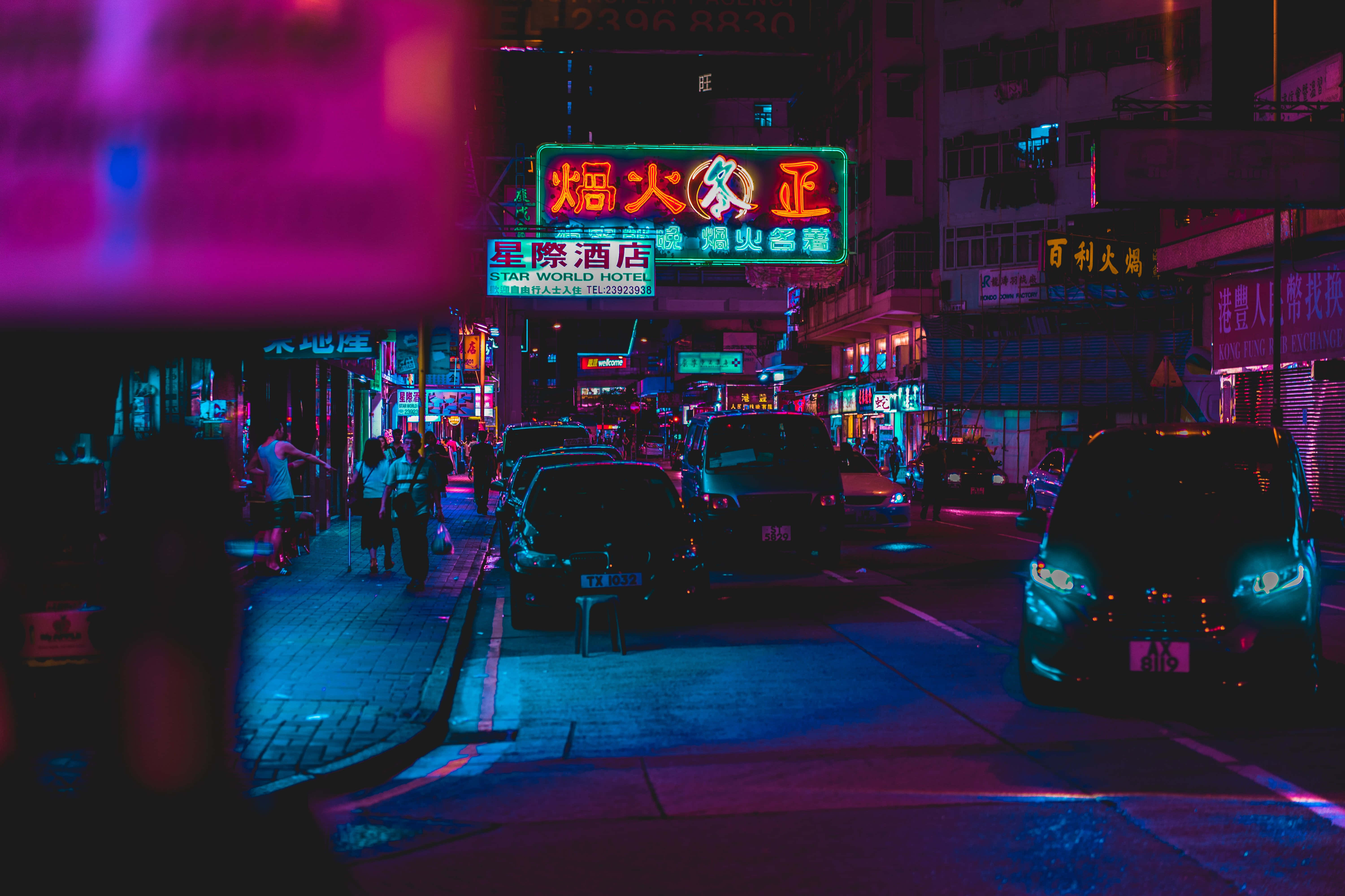 Night Street 桌布 壁紙 — 充滿活力的霓虹燈在夜間繁華的城市街道上閃爍著粉紅色和藍色，街道上停著汽車和行人。