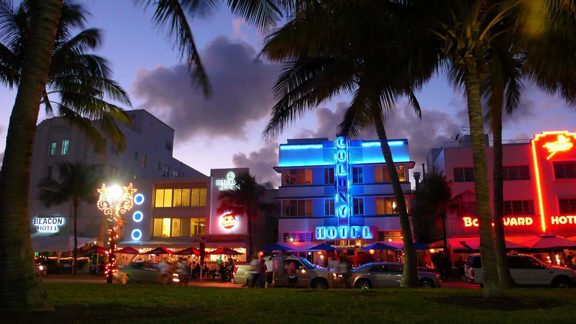Miami 桌布 壁紙 — 充滿活力的霓虹燈在裝飾藝術風格的酒店上閃耀，棕櫚樹在黃昏時分勾勒出邁阿密海灘熱鬧的街道。