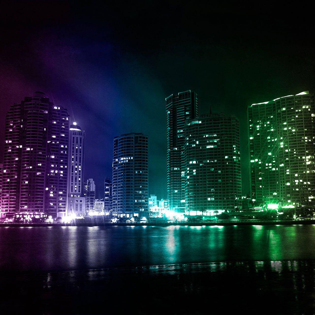 City Night 桌布 壁紙 — 充滿活力的霓虹燈城市天際線在夜晚倒映在平靜的水面上，紫色和綠色的色調照亮了高聳的摩天大樓。