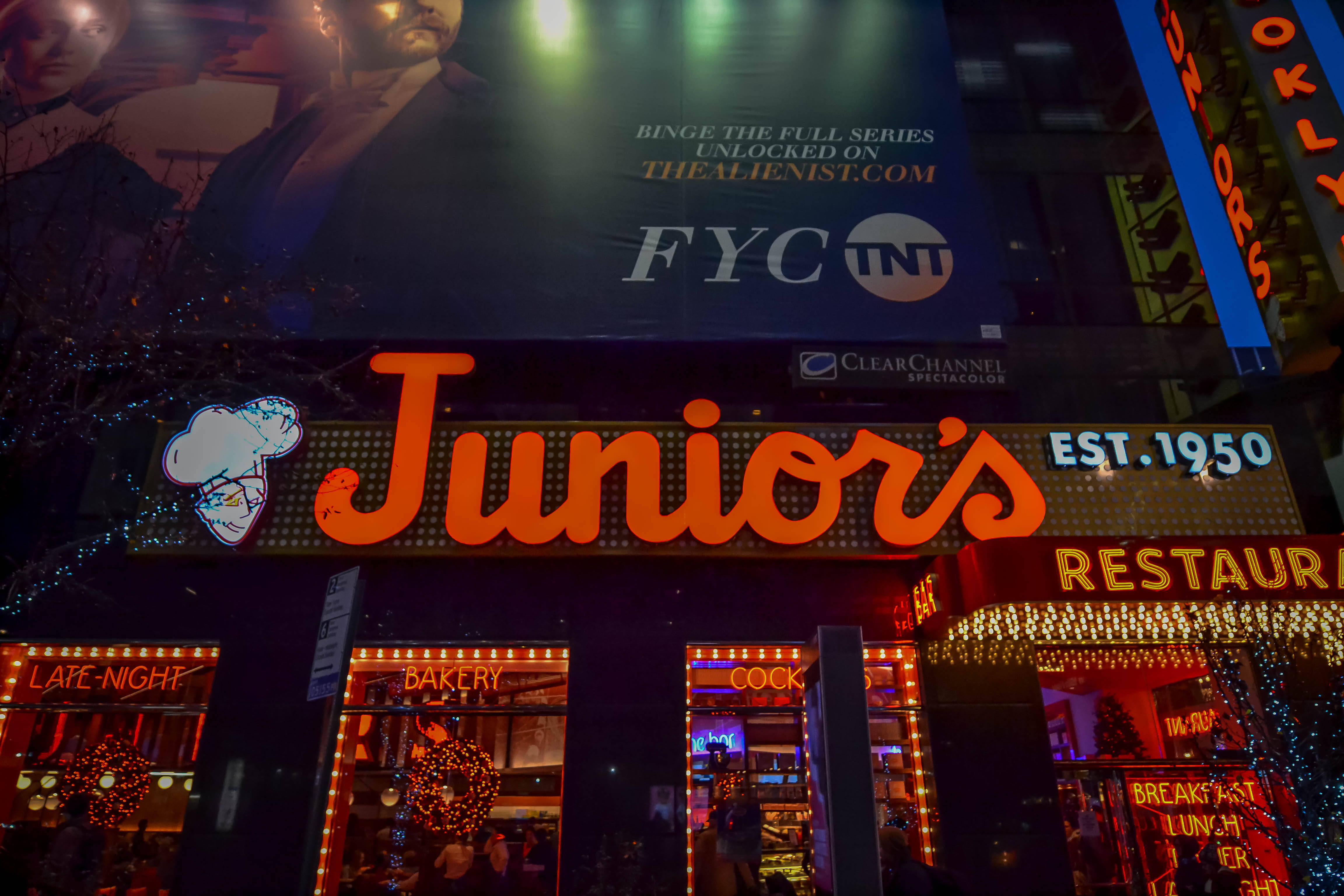 Nyc 桌布 壁紙 — 充滿活力的霓虹燈招牌在夜間照亮了 Junior's Restaurant，帶有節日燈光和上方的大型廣告牌。
