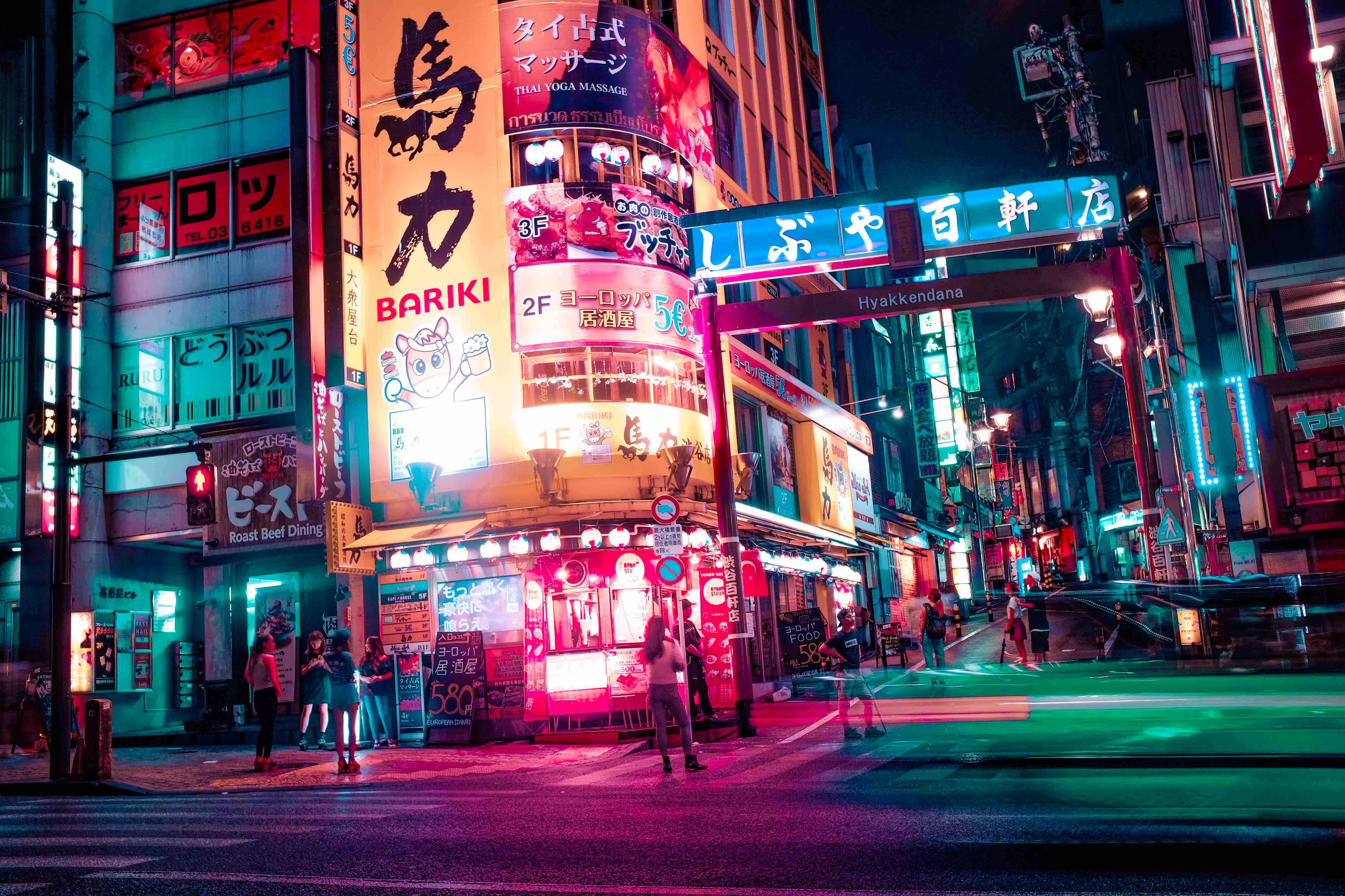 日本 桌布 壁紙 — 充滿活力的霓虹燈招牌照亮了夜晚繁忙的東京街道，粉紅色、綠色和藍色的燈光在潮濕的人行道上反射。