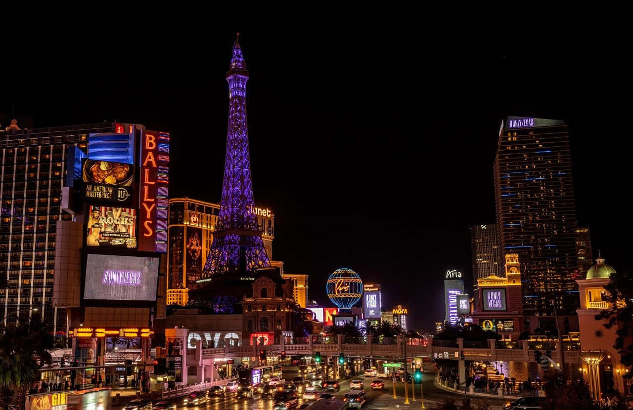 Nevada 桌布 壁紙 — 充滿活力的霓虹燈照亮了夜晚的拉斯維加斯大道，下方有發光的艾菲爾鐵塔複製品和繁忙的交通。
