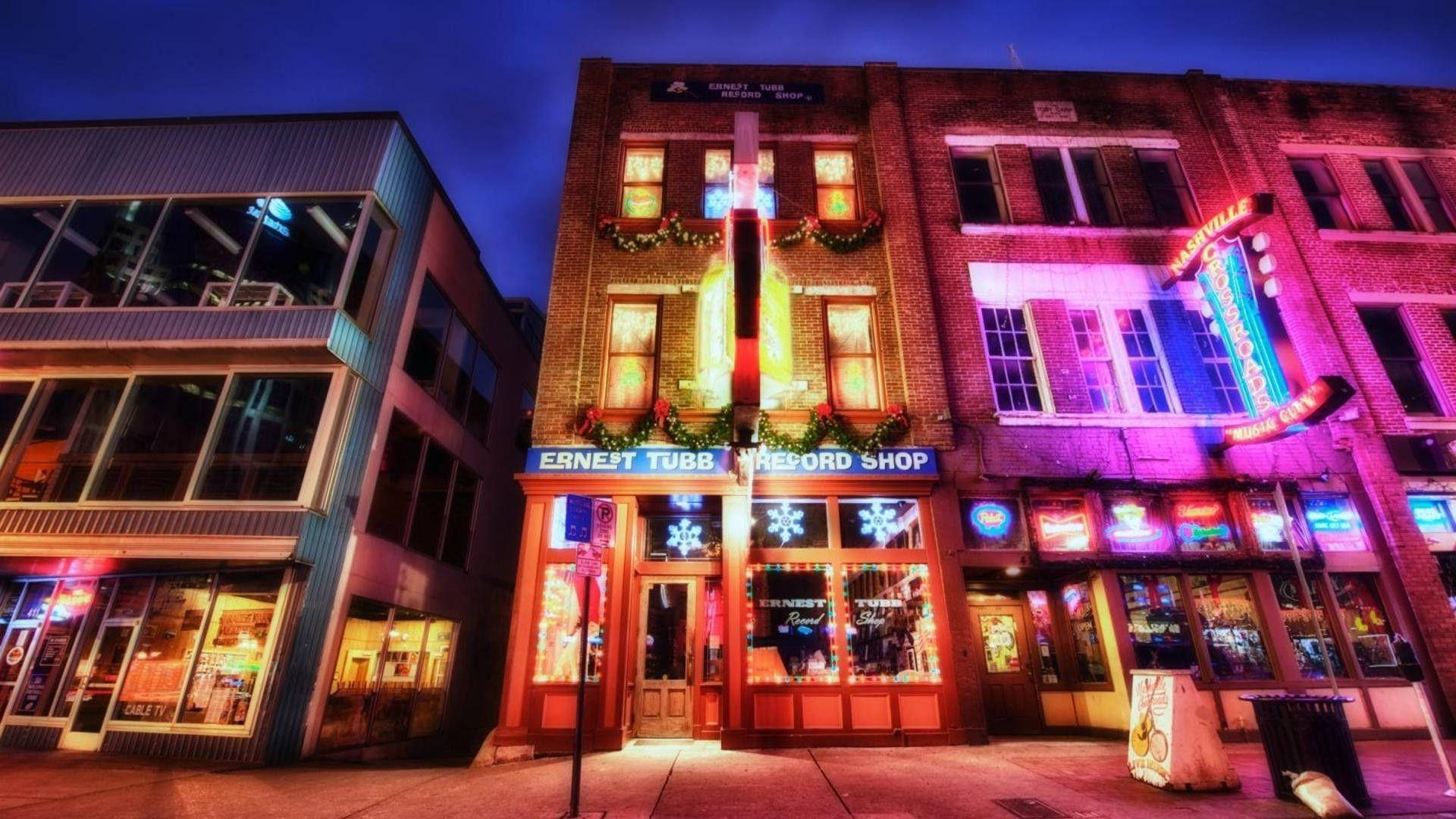 Building 桌布 壁紙 — 充滿活力的霓虹燈照亮了夜晚的節日城市街道，節日裝飾點綴著磚砌建築。