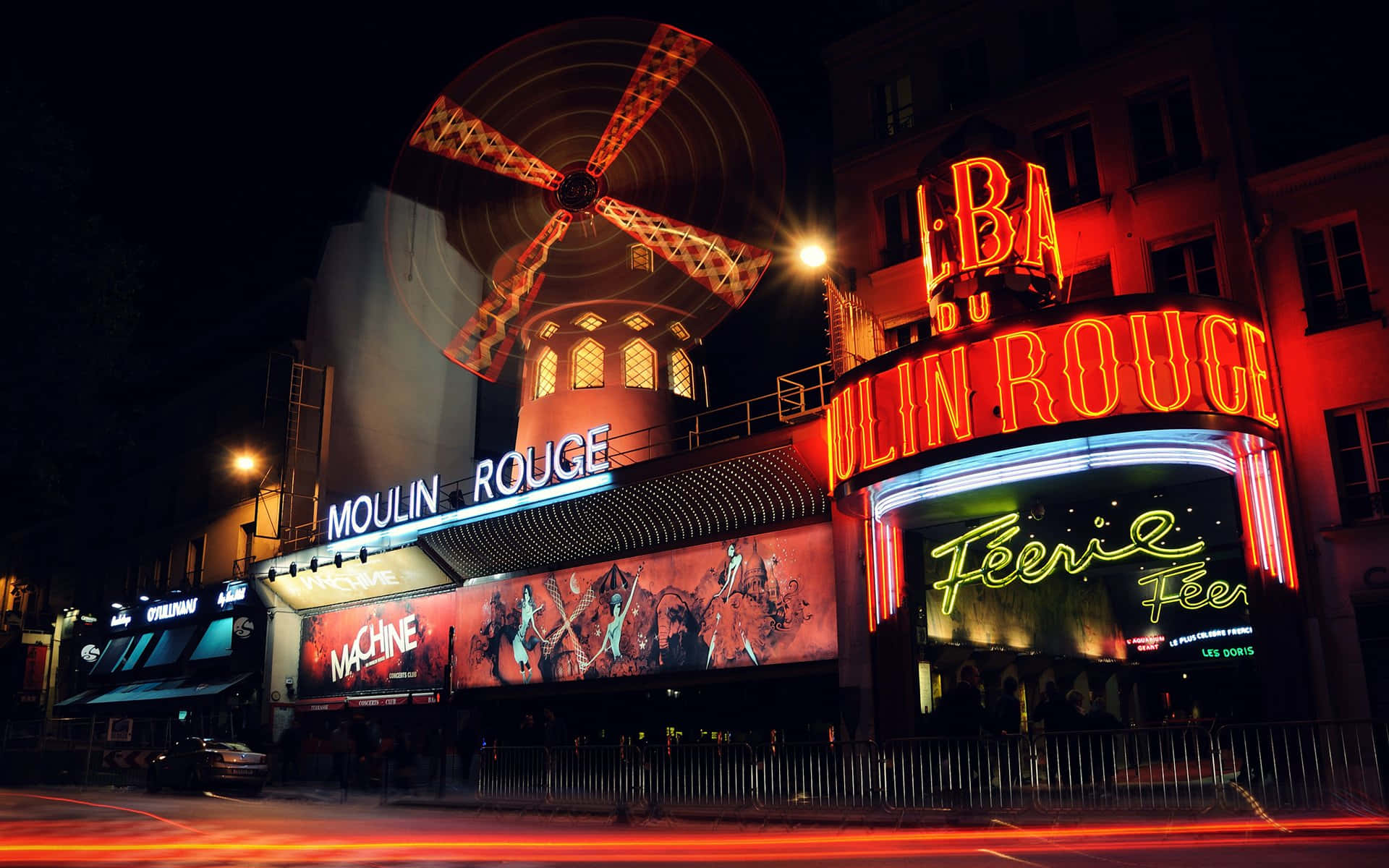 moulin rouge 桌布 壁紙 — 充滿活力的霓虹燈照亮了夜晚的紅磨坊，閃爍的風車和繁華的街景。