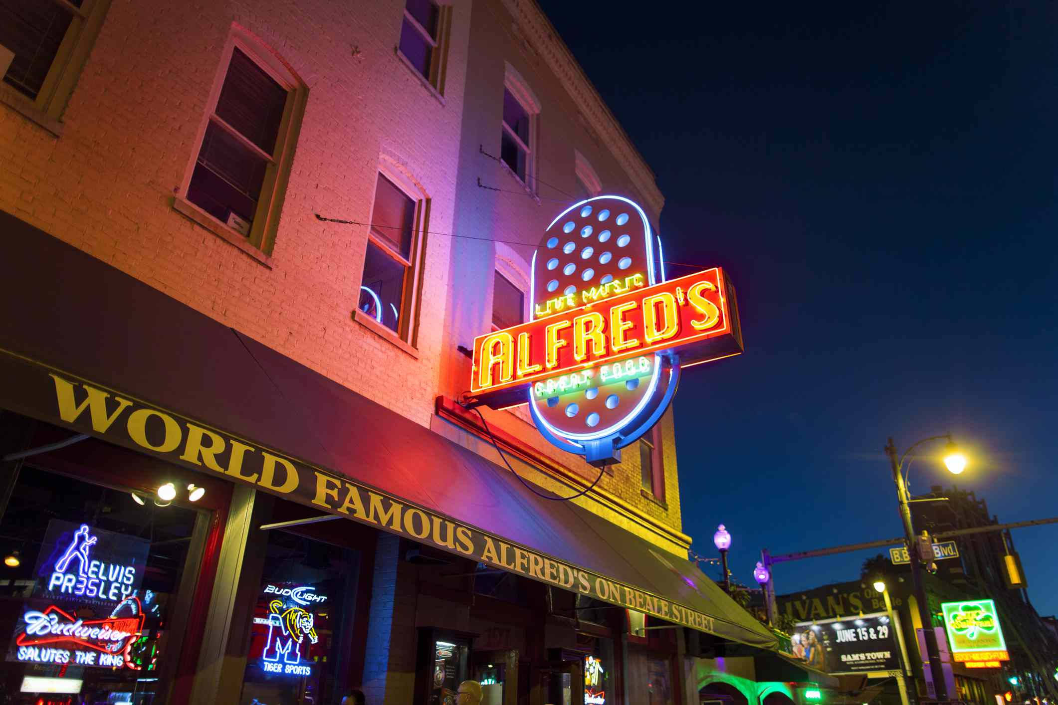 Tennessee 桌布 壁紙 — 充滿活力的霓虹燈照亮了夜晚繁華的城市街道，Alfred's 餐廳和貓王紀念品在磚砌建築的映襯下閃閃發光。