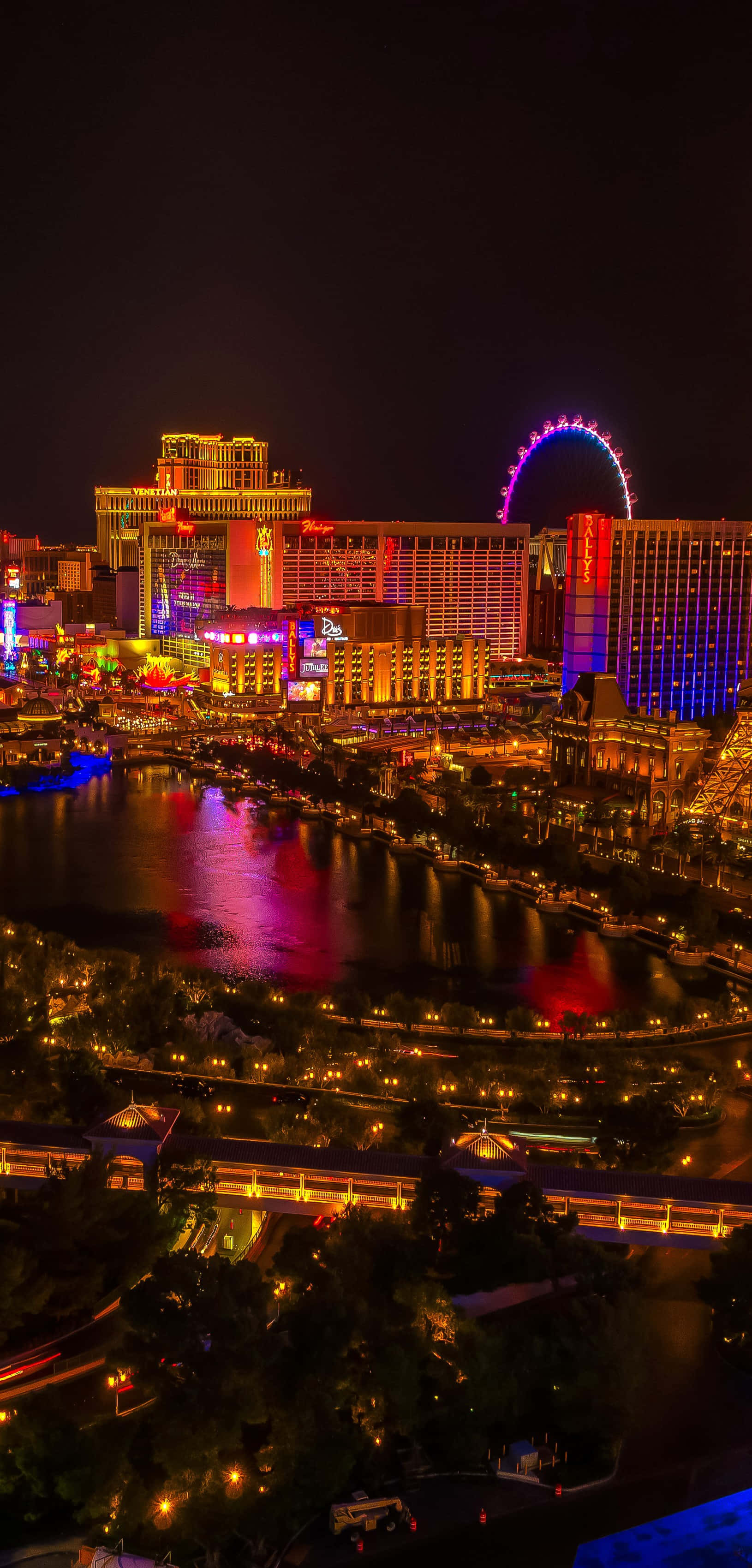 Las Vegas Phone 桌布 壁紙 — 充滿活力的霓虹燈照亮了夜間的拉斯維加斯大道，High Roller摩天輪在閃爍的飯店和反射的水面上方發光。