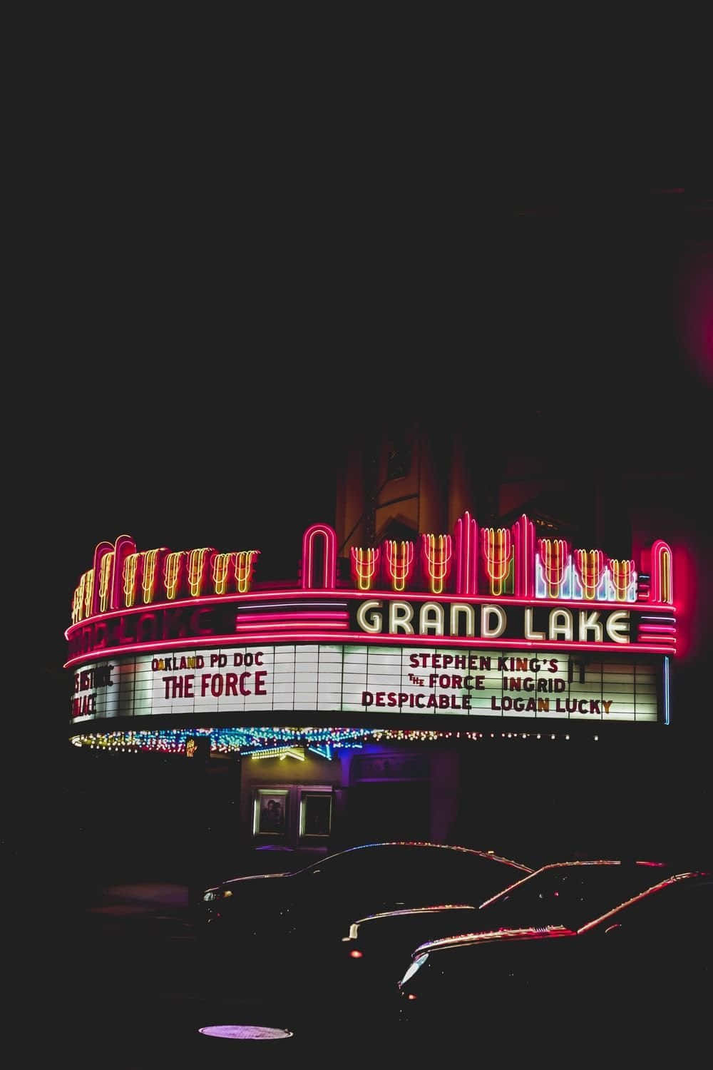 Aesthetic Grunge Neon Signs 桌布 壁紙 — 充滿活力的霓虹燈照亮的大湖劇院招牌在夜晚閃耀，電影標題映襯著黑暗的天空和下方停放的汽車。