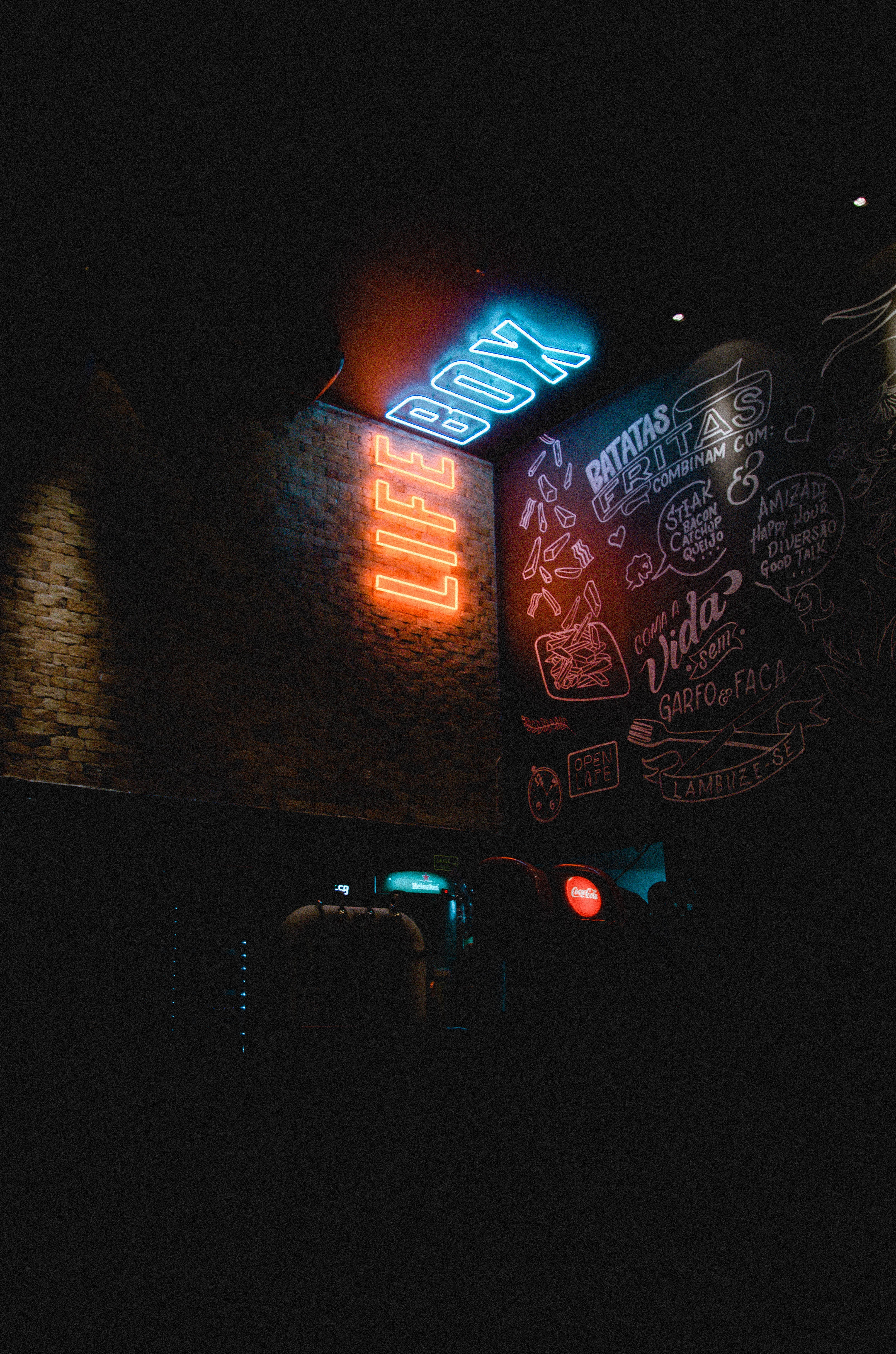 neon sign 桌布 壁紙 — 充滿活力的霓虹燈牌在黑暗的磚牆上發出橙色和藍色的光芒，營造出熱鬧的夜生活氛圍。