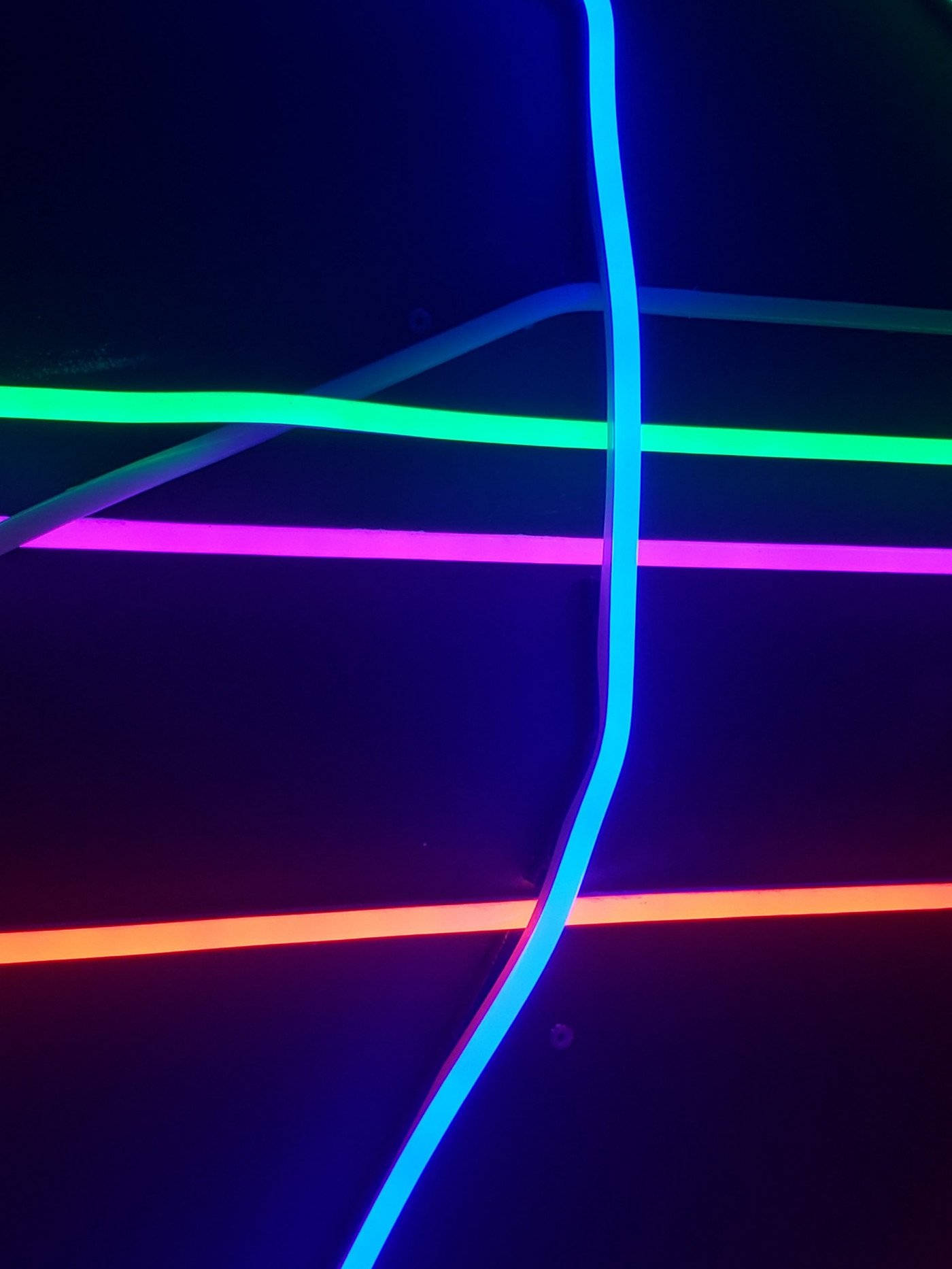 Neon Light 桌布 壁紙 — 充滿活力的霓虹燈管，以藍色、綠色、紫色和橙色在深色背景上發光，形成動態的抽象圖案。